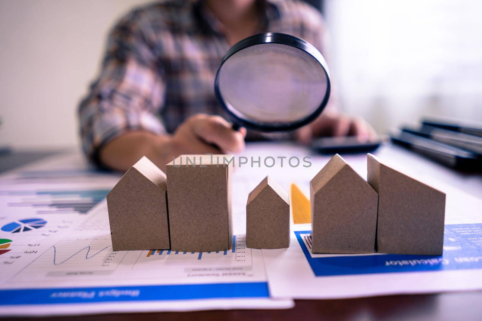 Real estate or House Appraisal using calculator and holding a magnifying glass over the model of a wooden house. Property valuation or appraisal and Search for housing concept.