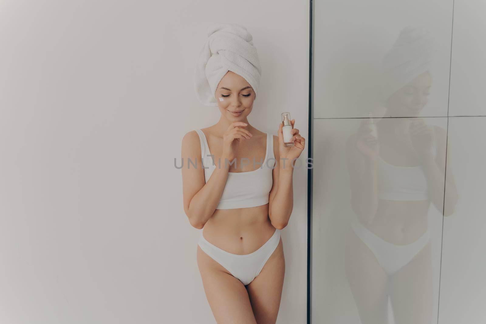 Young girl posing with cosmetic moisturizing face cream or serum in hand isolated over light wall in bathroom by vkstock