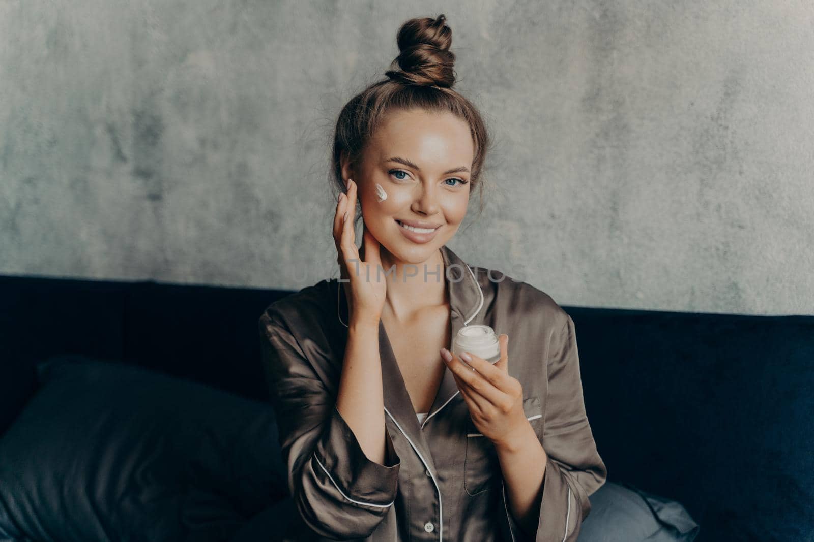 Beautiful brunette female prepares herself for morning make up, applying face cream by vkstock