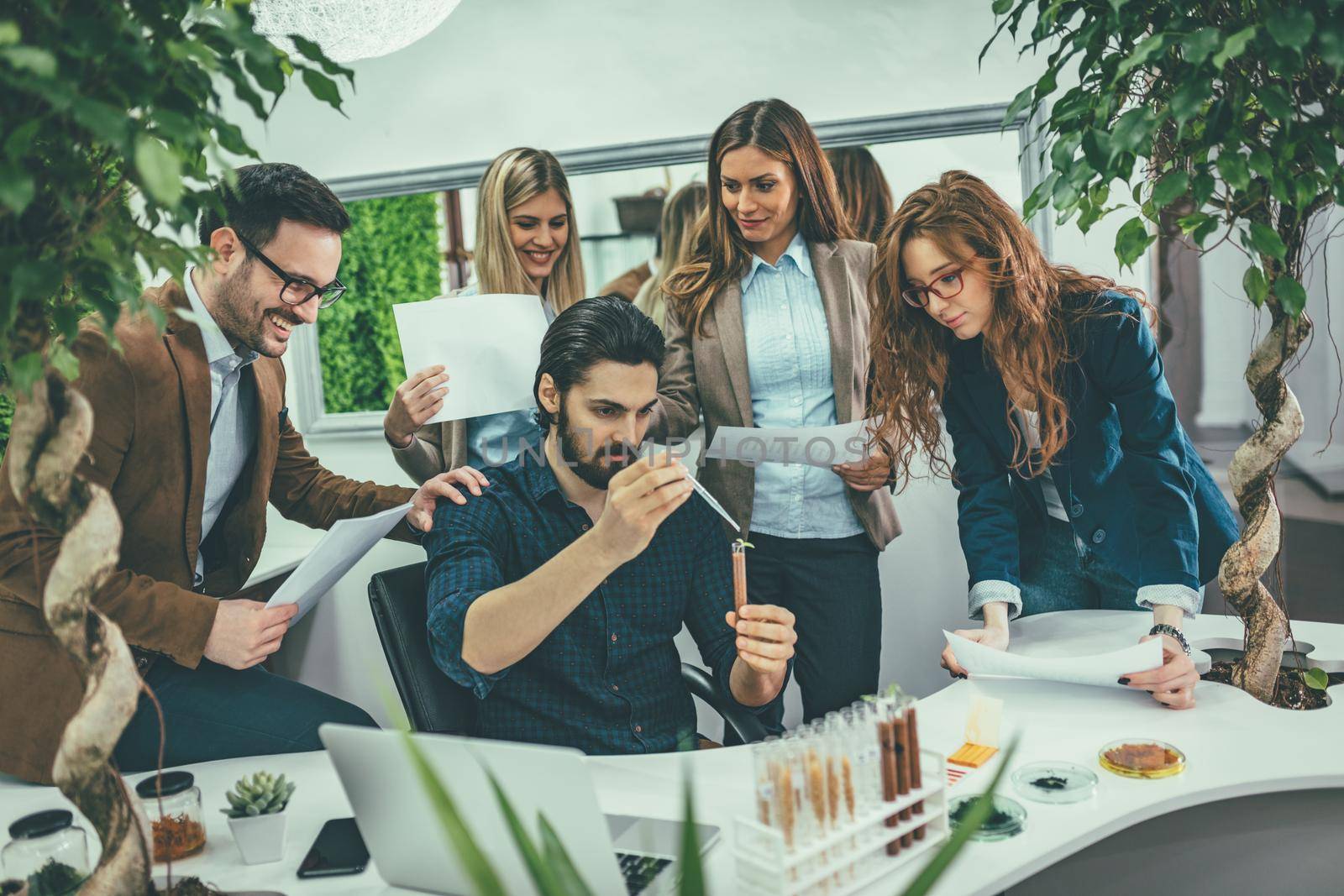 Team of university biologists analysing the sample of plant in the lab tube, watering it with drops of nutritious fluid.  