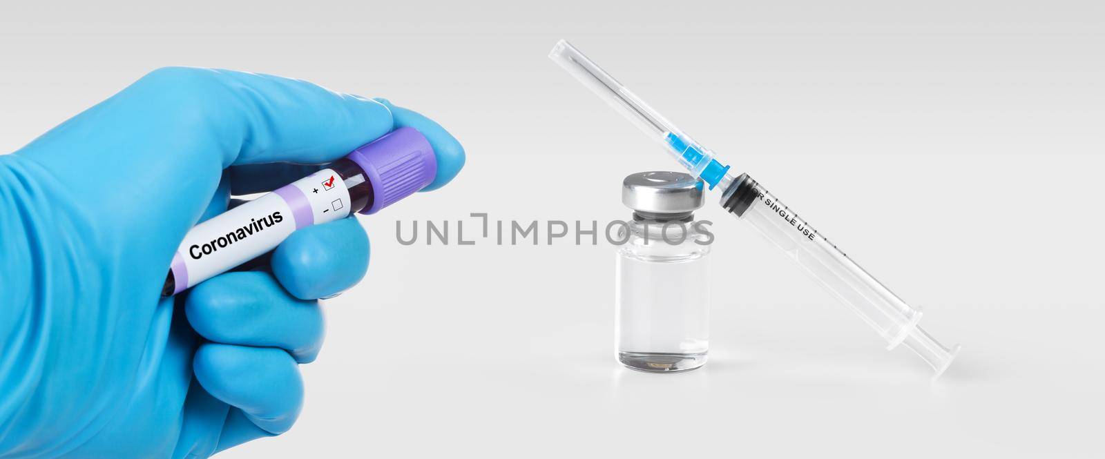 Hand holding viol with Coronavirus 2019-nCoV Blood Sample. Medical syringe and a bollte with vaccine on the background. by Taut