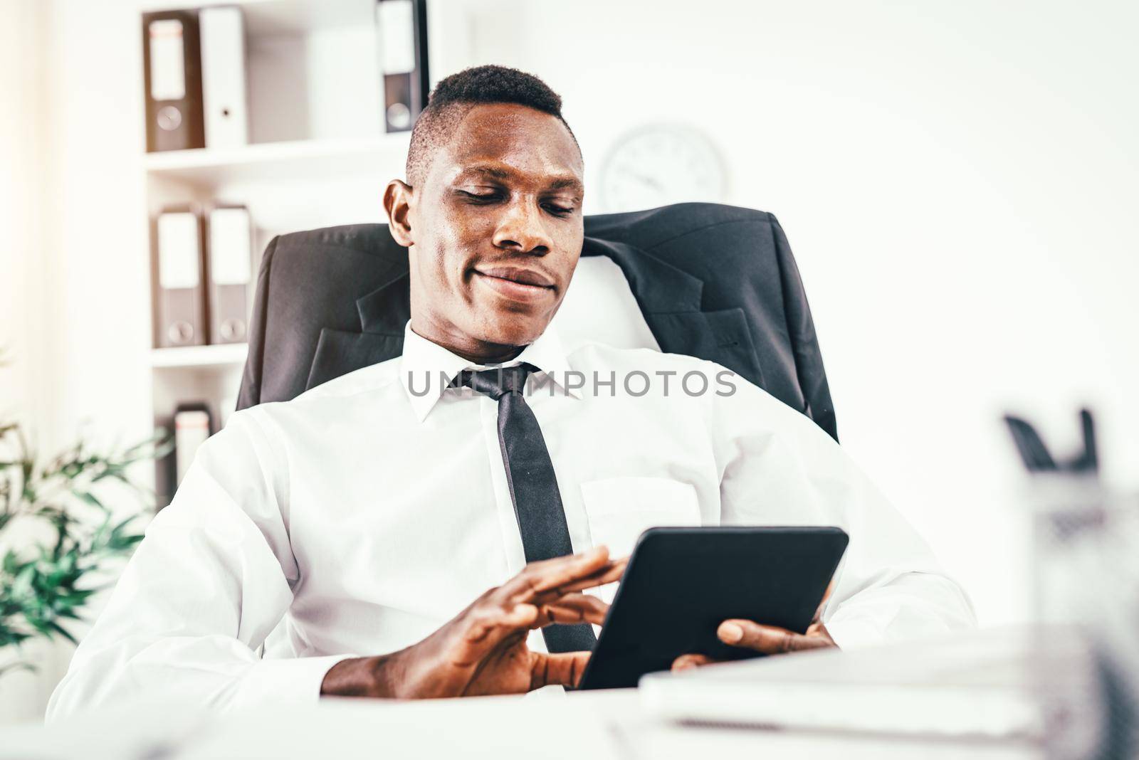 Satisfied African businessman working on digital tablet in modern office.