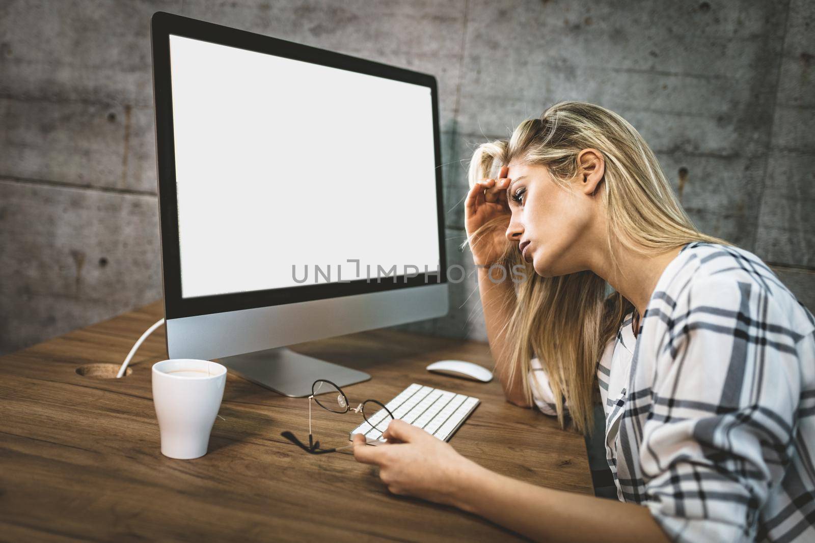 Young handsome frustrated and stressed business woman sitting at the office front a computer and holding head.