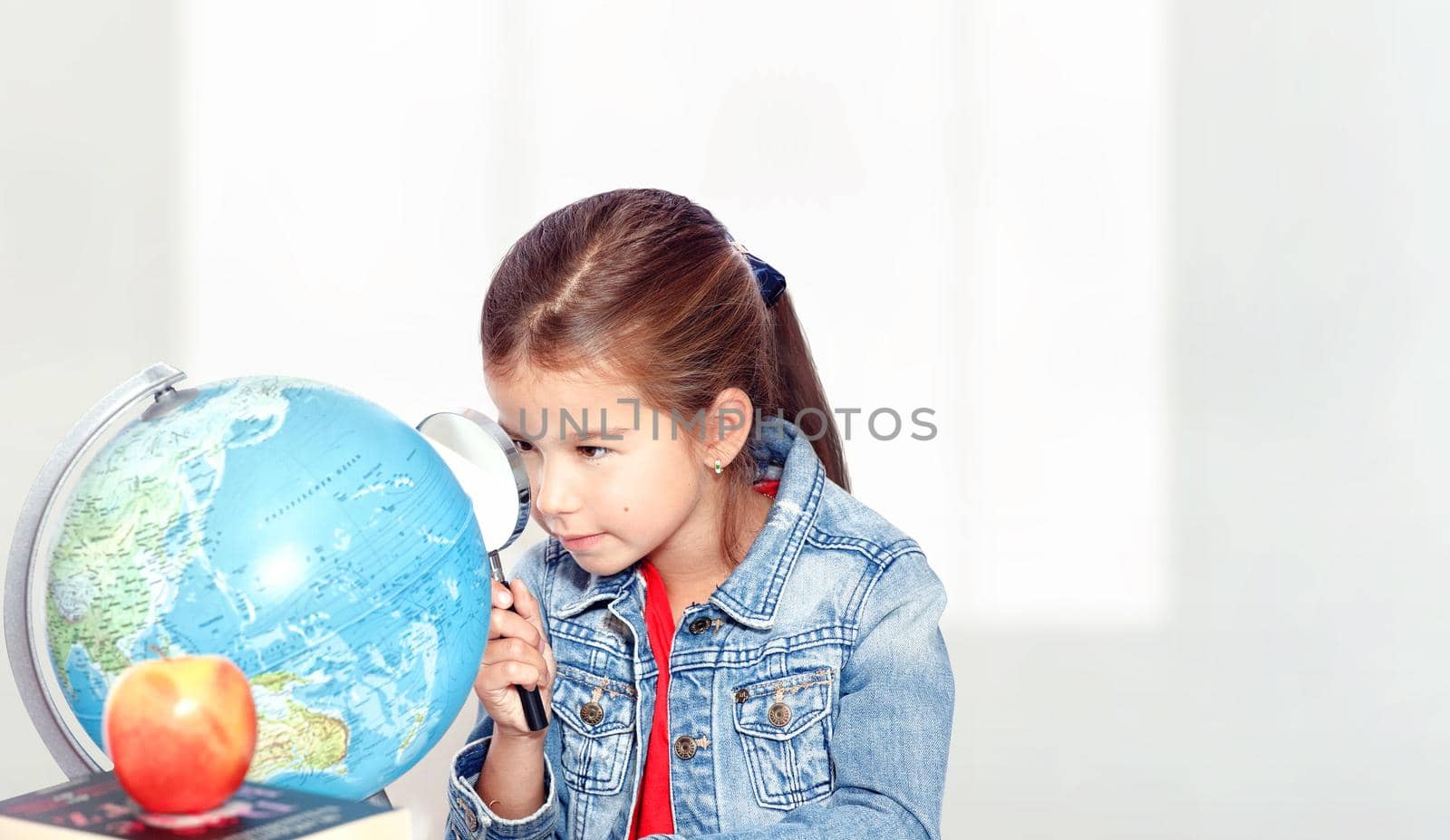 Curious little girl looking through magnifying glass on globe by Taut