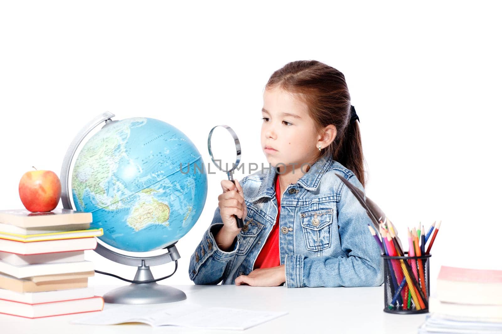 Curious little girl looking through magnifying glass on globe by Taut