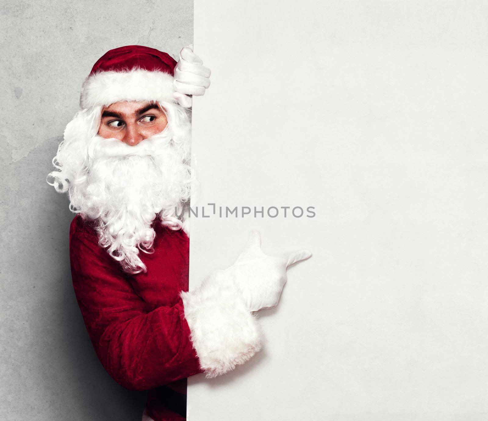 Happy Santa Claus pointing in blank wall with copy space by Taut
