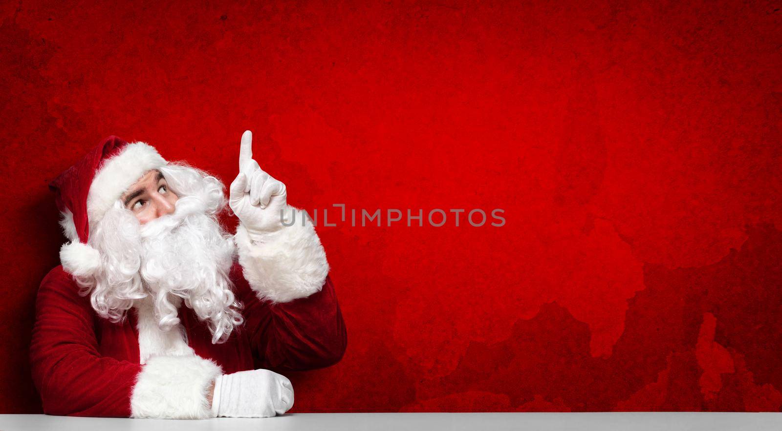 Happy Santa Claus pointing in blank wall with copy space by Taut