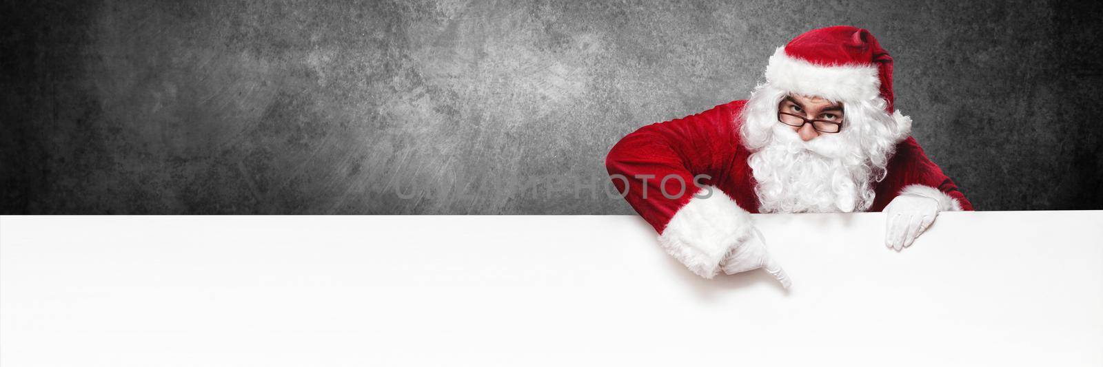 Happy Santa Claus pointing in blank wall with copy space by Taut