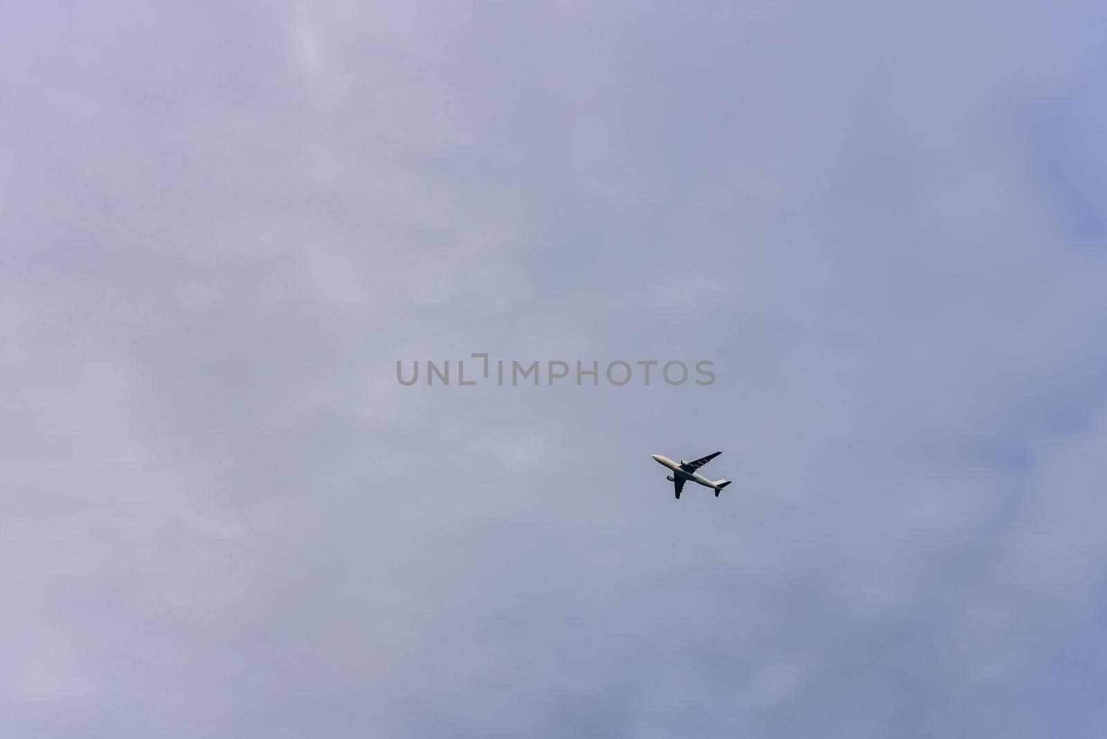 Passenger plane is flying far away against the blue summer and cloudy sky with copy space.