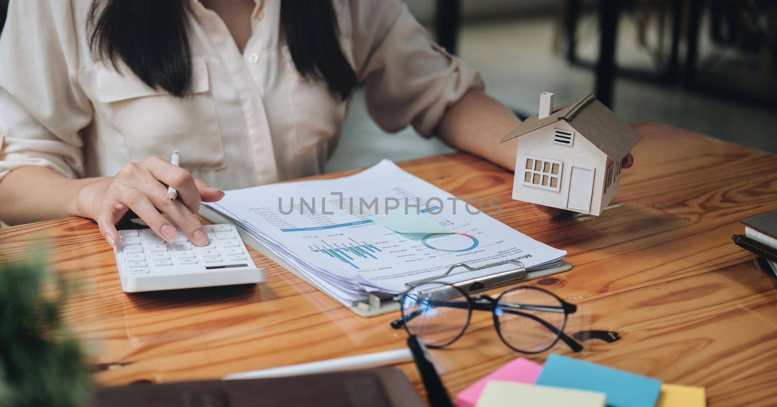 businesswoman with house model doing finances and calculate about cost to real estate investment and in other, tax system. Business Financing Accounting Banking Concept by nateemee