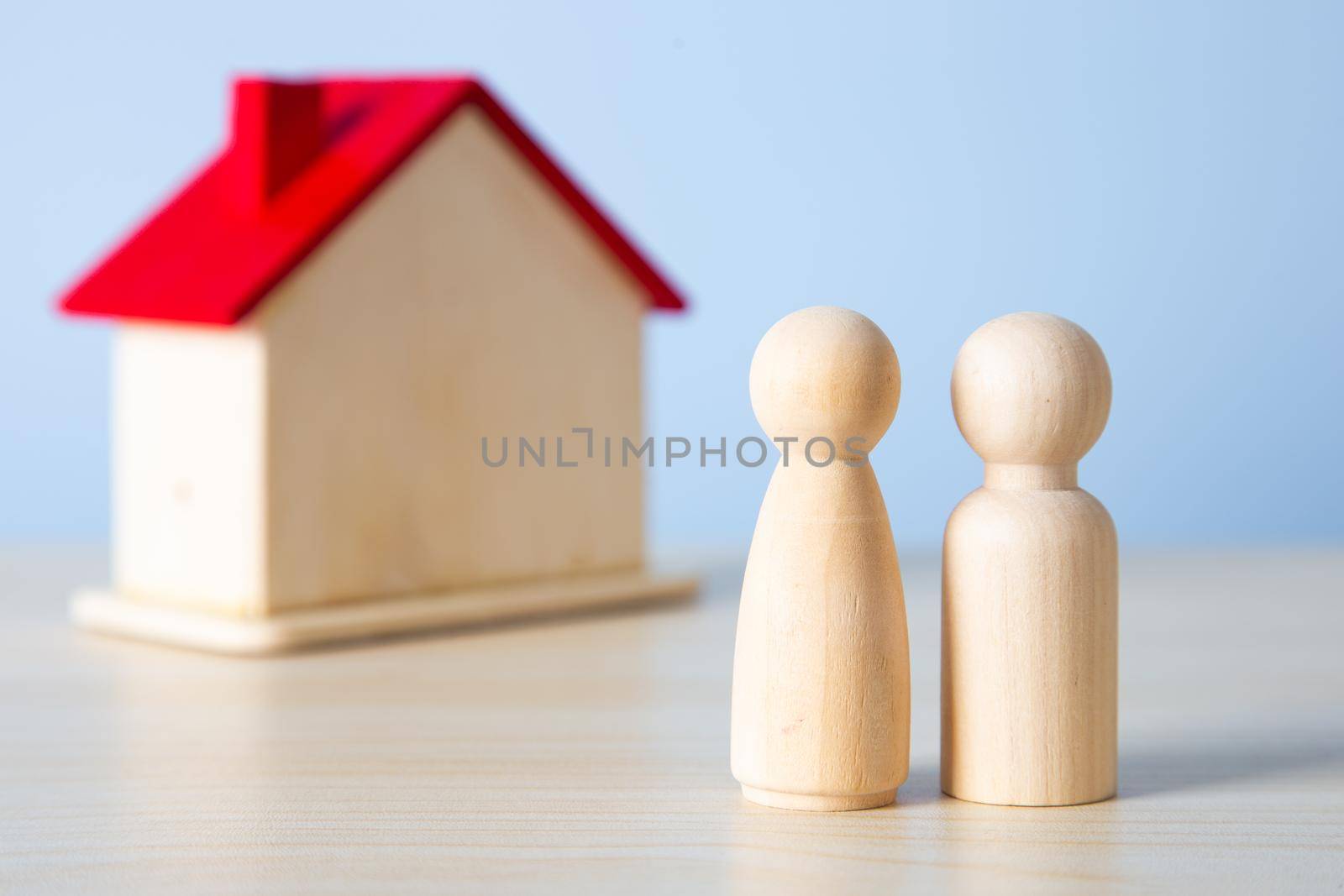 Wooden doll family stands in front of house model.