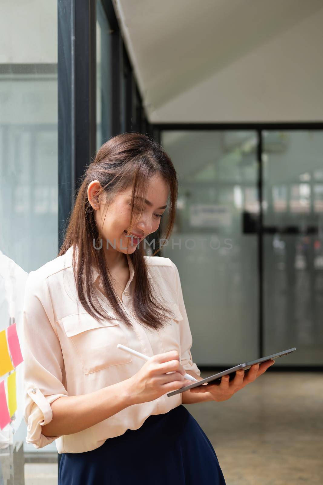 Portrait happy woman manager holding tablet and standing in modern office. Asian female using stylus with tablet.