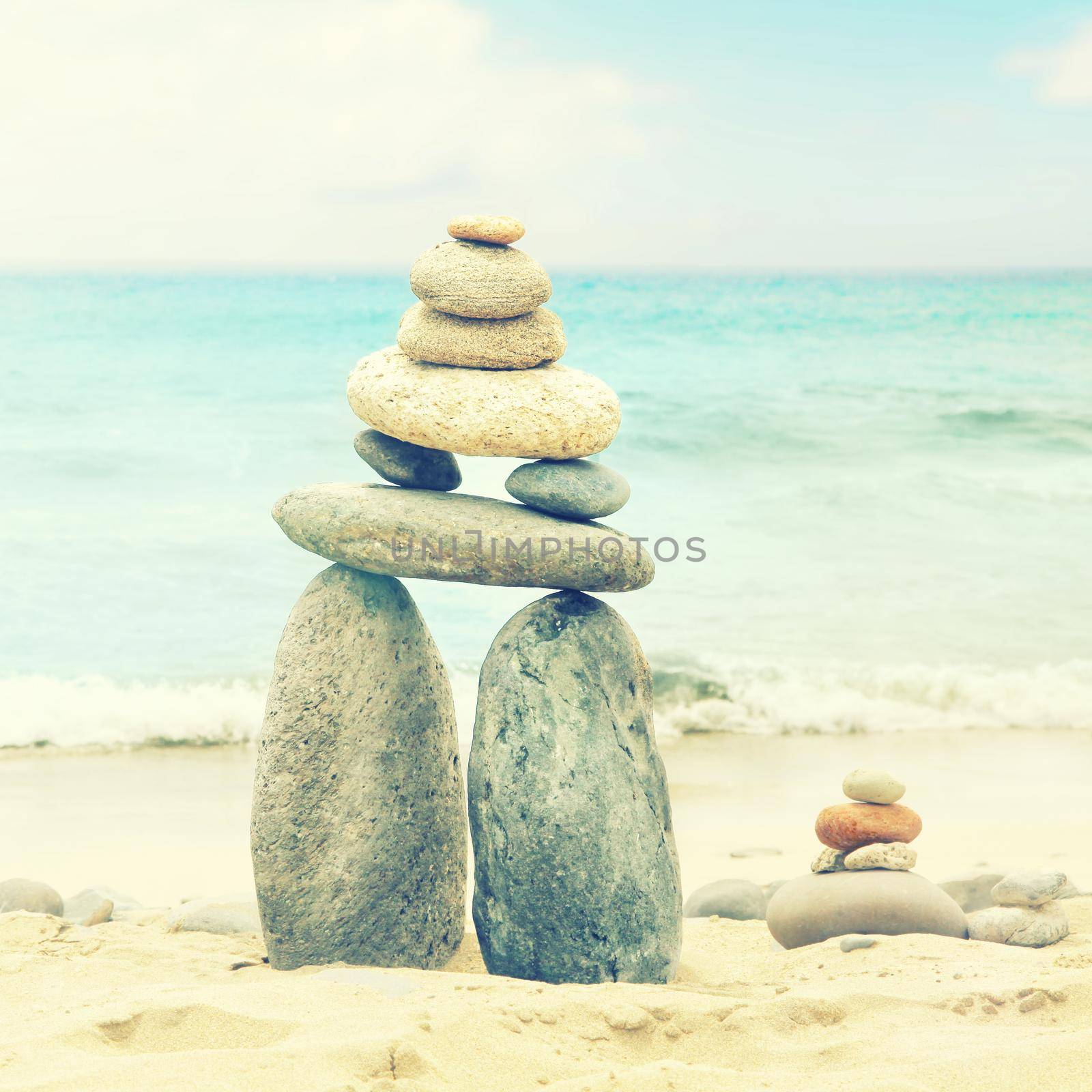 Balanced stones on a pebble beach during sunset. by Taut