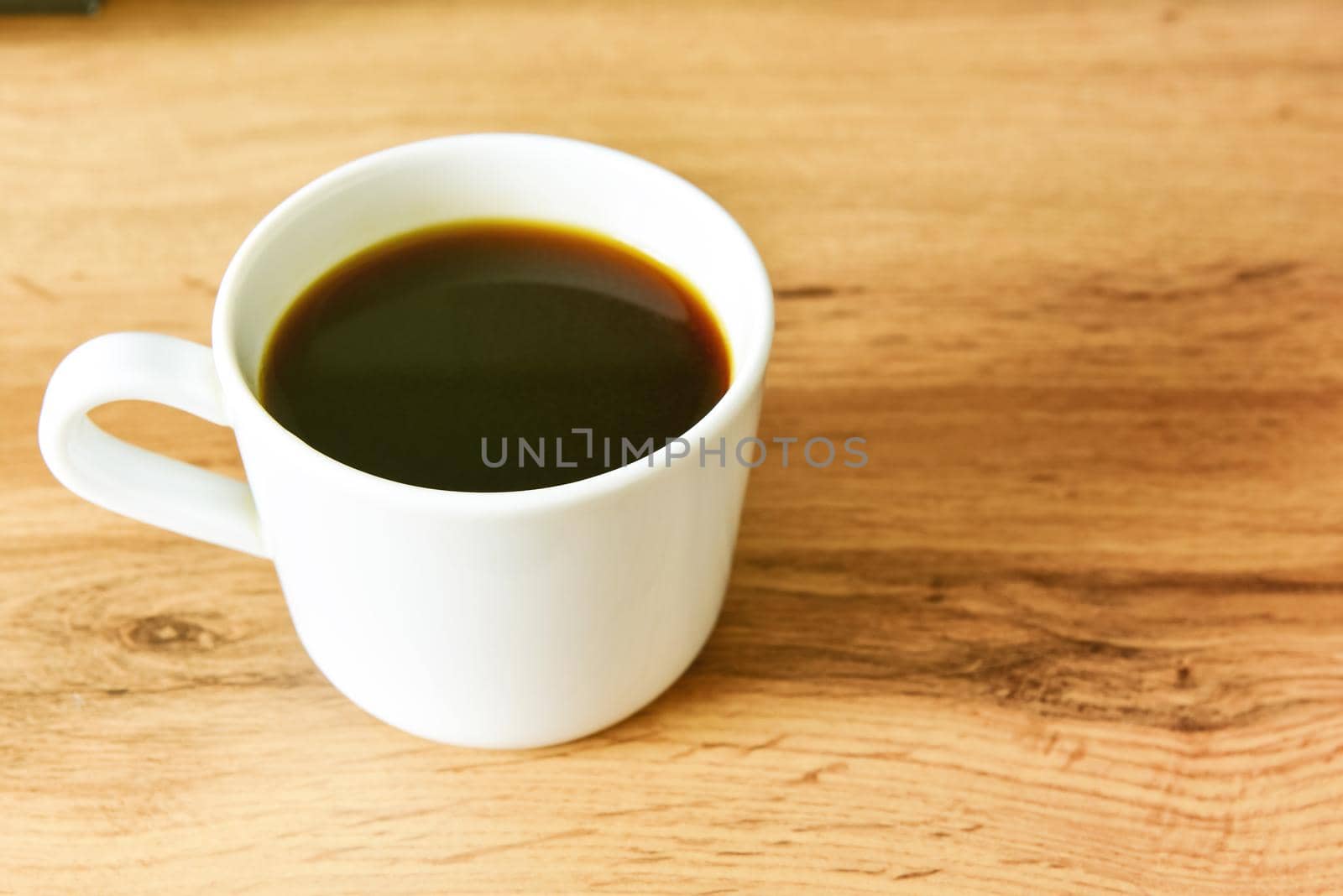 White cup of strong black coffee on wooden surface close up.