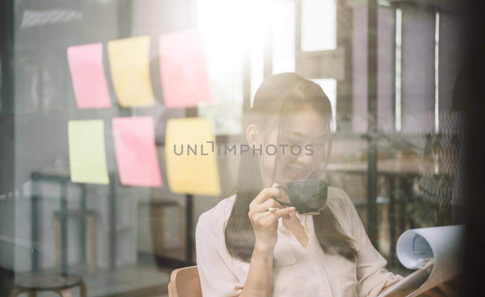 shot of asian business woman working during drinking offee with financial document at her office by nateemee