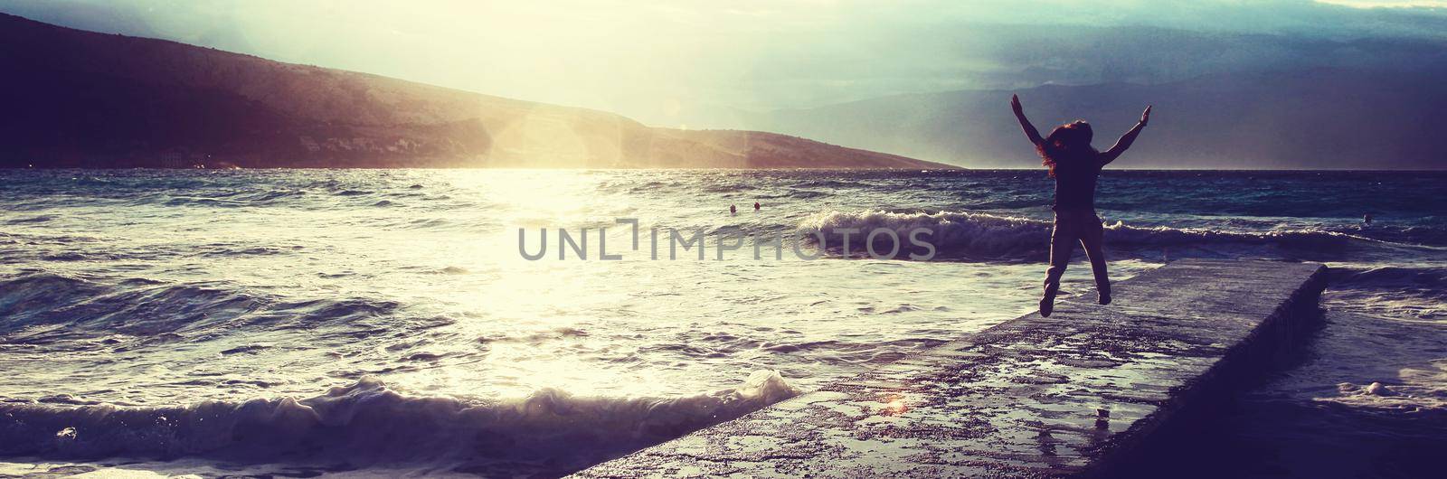 Feeling of freedom concept. Woman jump on pier facing to the sea with big waves.