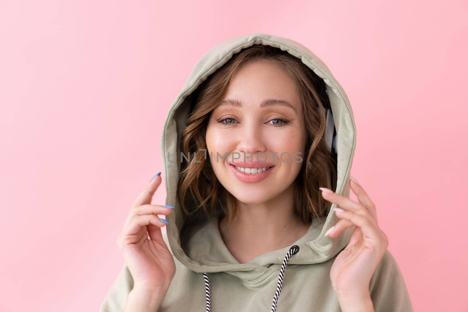Happy teeth smile woman holds hood with his hands Caucasian female enjoy dressed oversize hoodie pink background close up portrait
