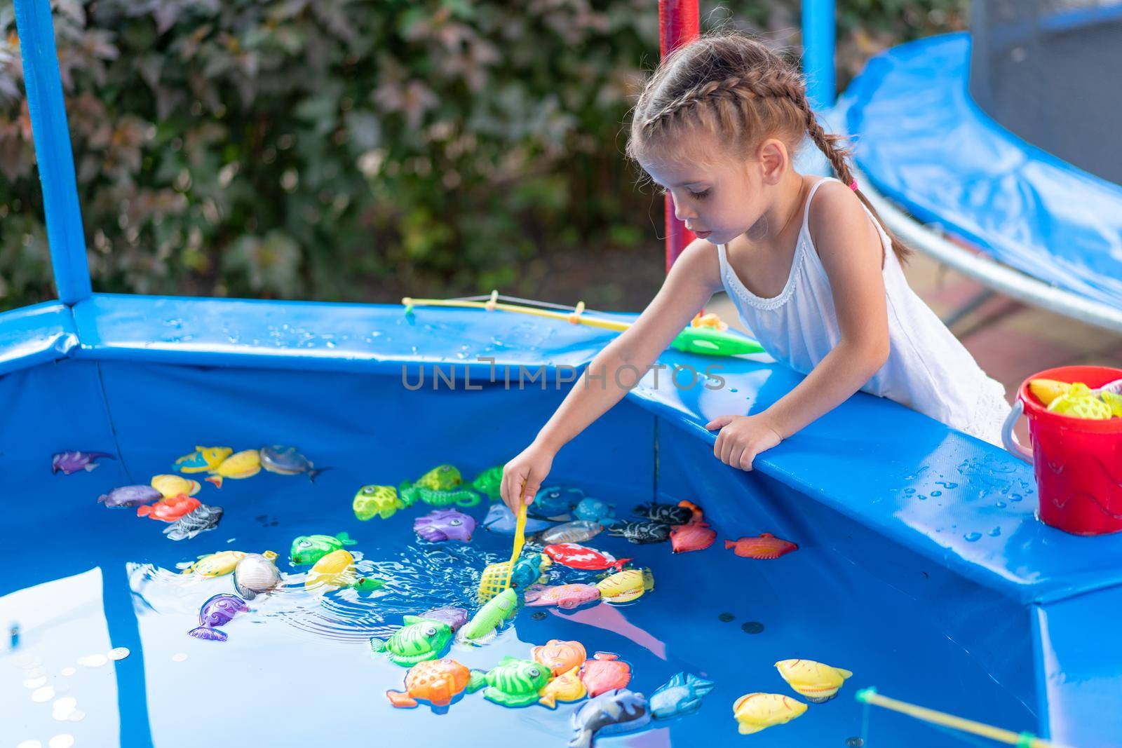 Child Fisher Catching Plastic Toy Fish On Pool Amusement Park Summer Day Little Girl Have Fun On Fishing Carnival Festival Entertainment For Children