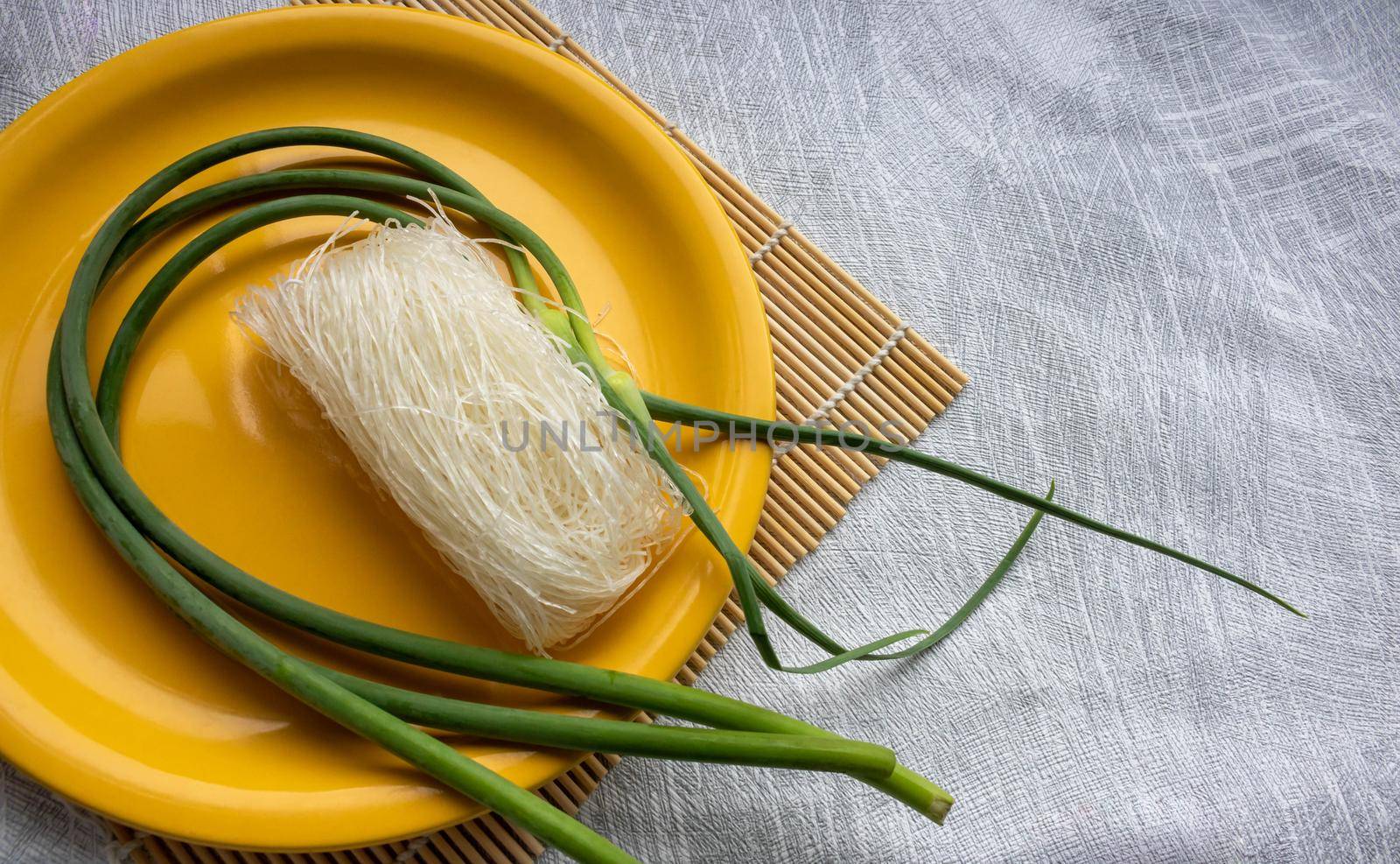 Green onion arrows and bean noodles lie on a yellow plate on a gray background.