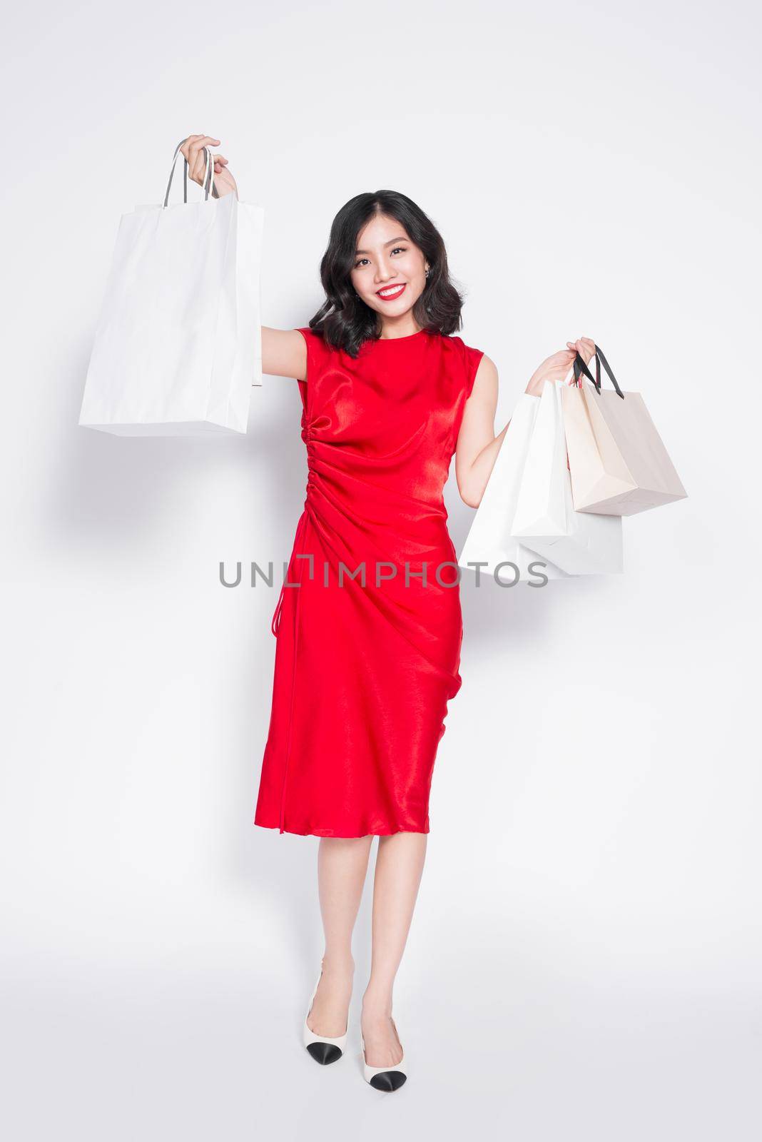 Full length portrait of asian cheerful woman holding colorful shopping bags and posing by makidotvn