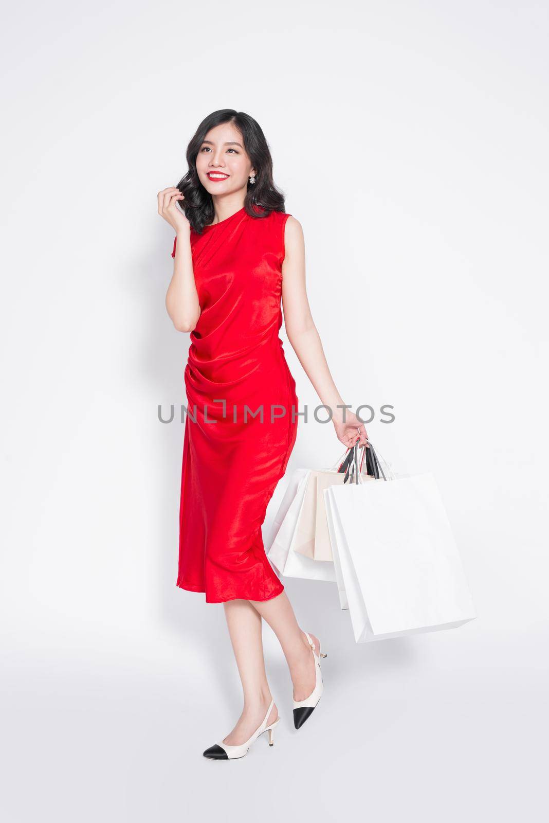 Full length of cheerful fashionable asian woman wearing a red dress with shopping bags by makidotvn