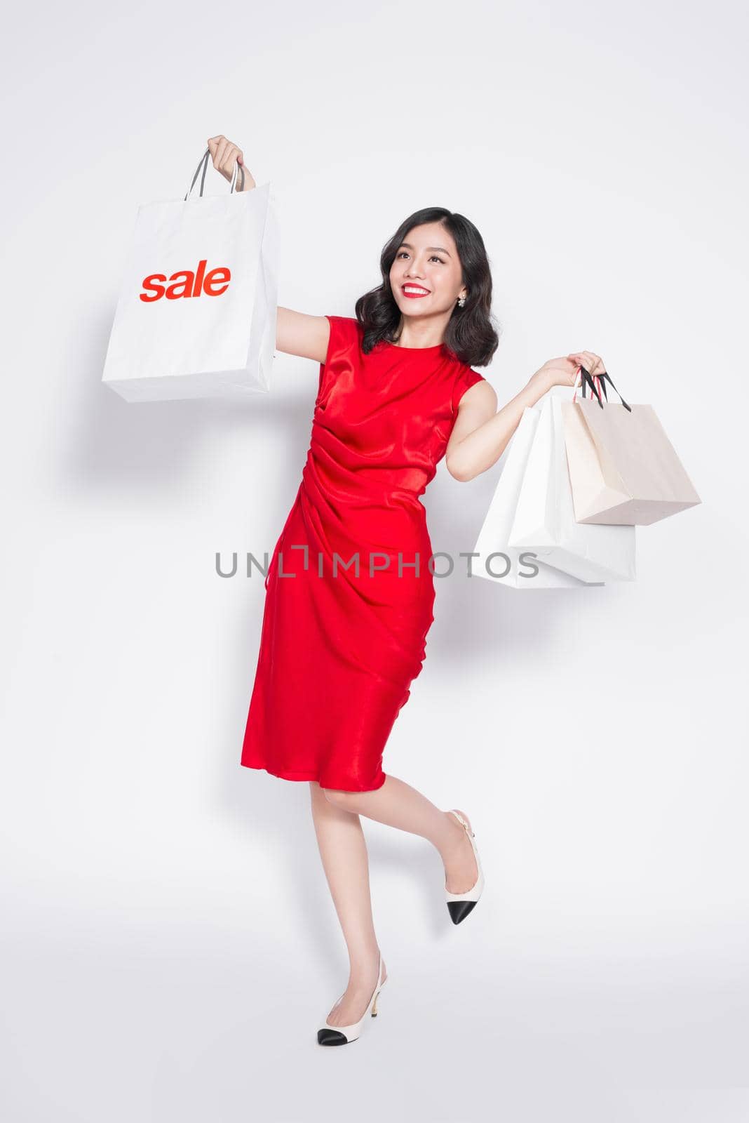 Full length of cheerful fashionable asian woman wearing a red dress with shopping bags by makidotvn