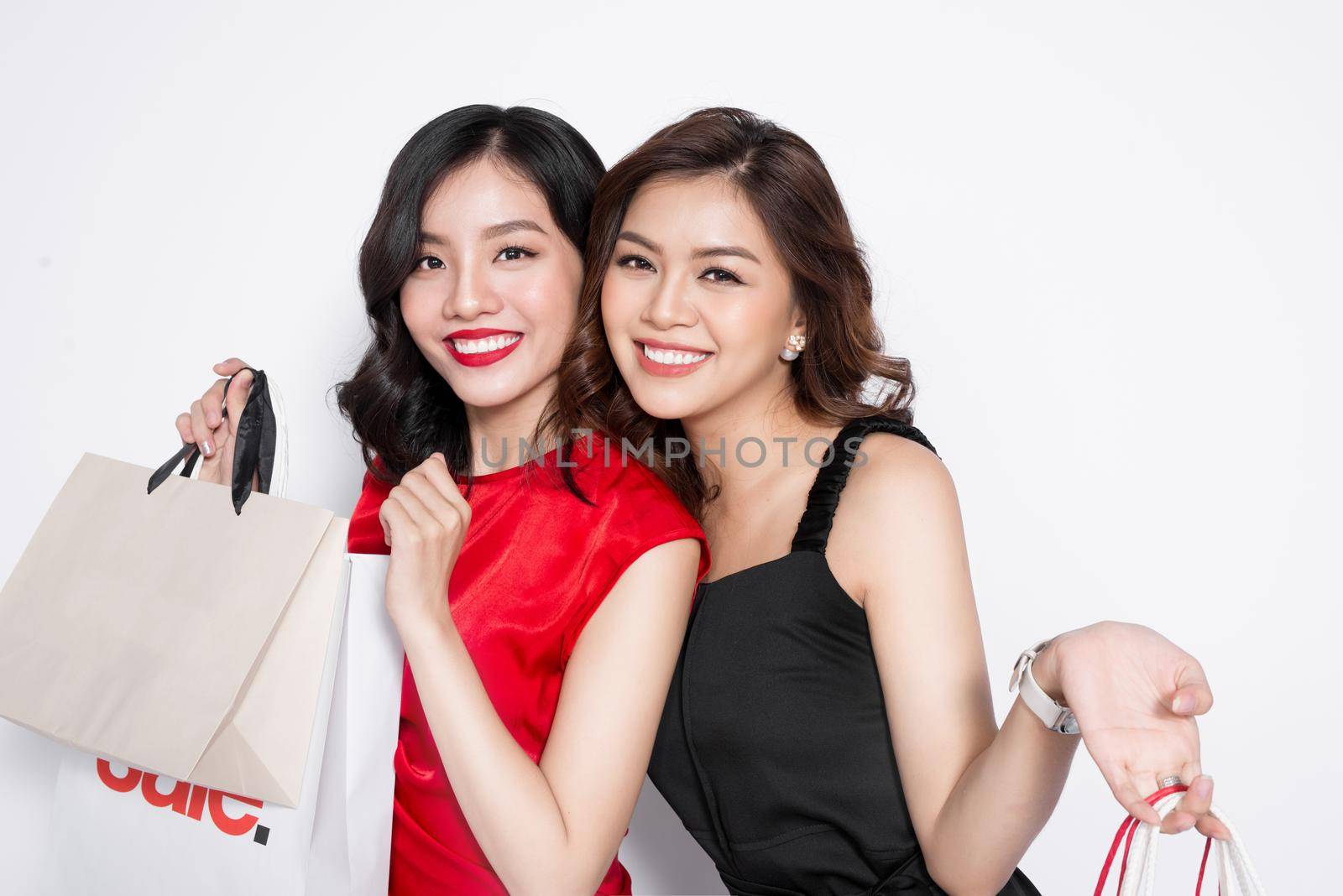 Two happy attractive young women with shopping bags on white background