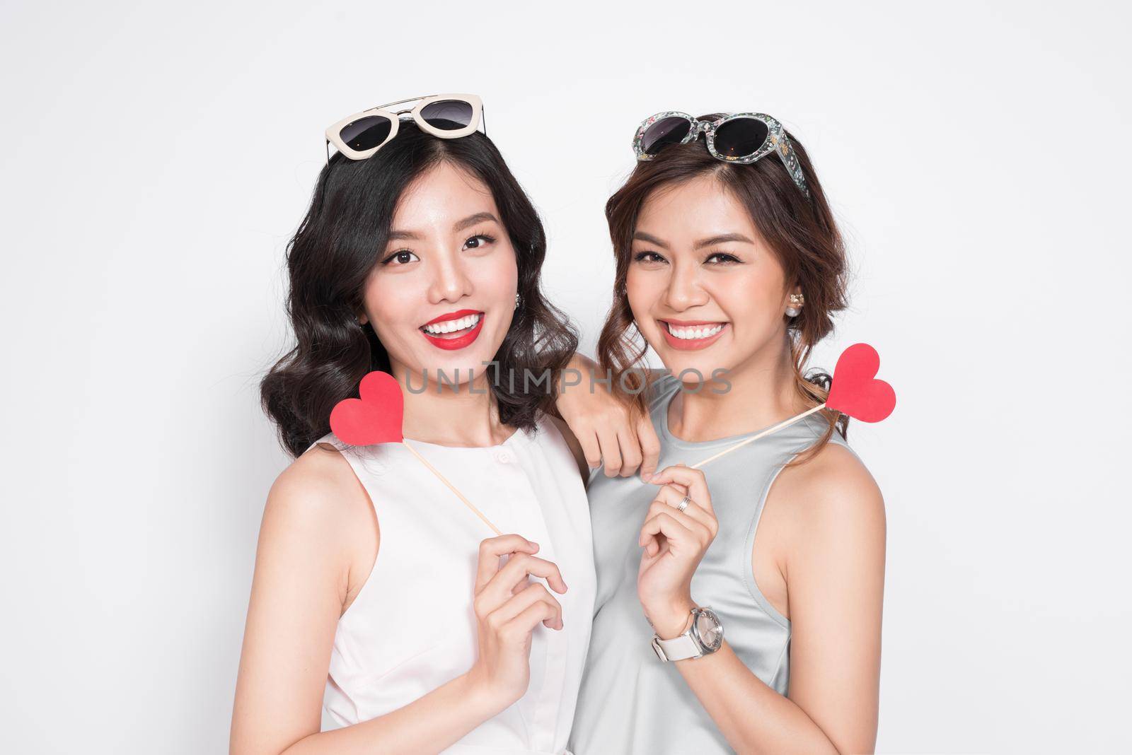 Two fashionable women in nice dresses standing together and holding red heart shape.