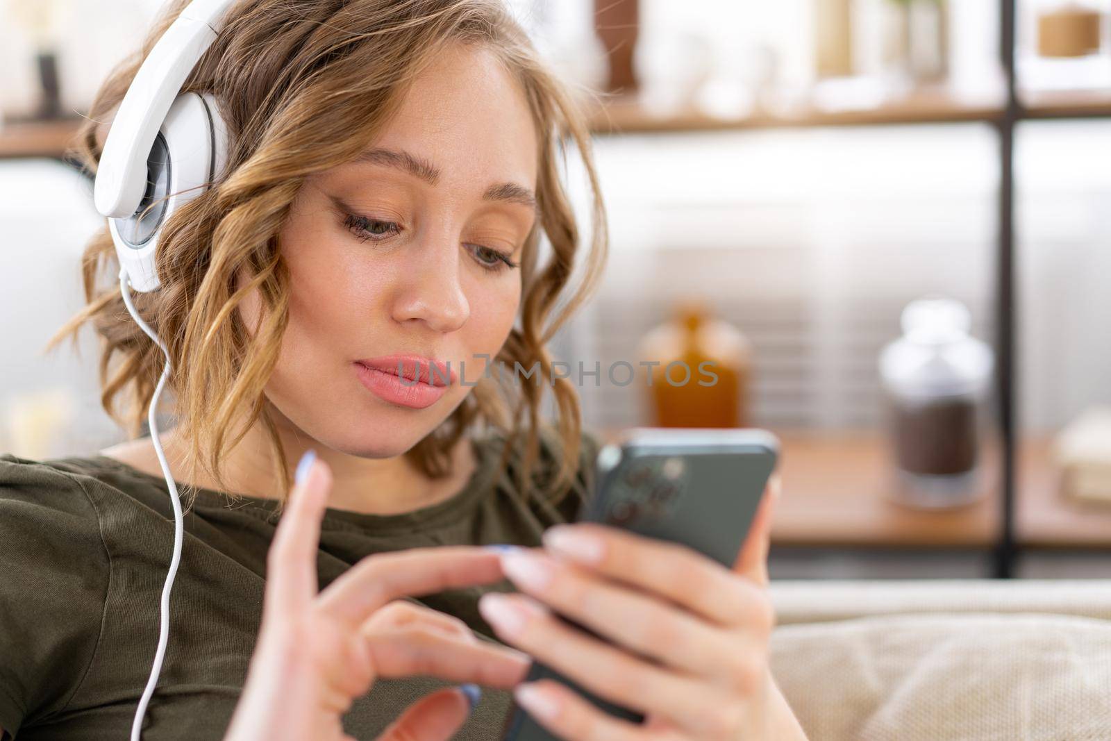 Woman listen music headphones holding smartphone in hand Caucasian female enjoy podcast or audio books while restin on couch close up portrait