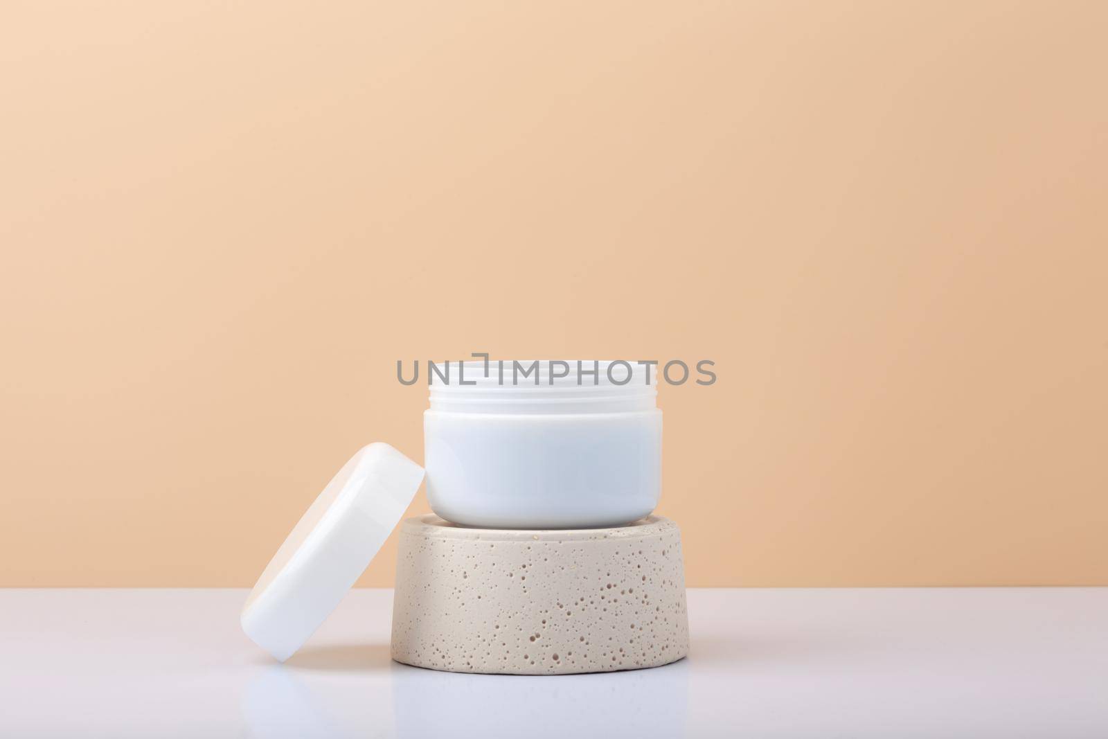 White cosmetic jar on gypsum podium against pastel beige background with copy space. Concept of organic natural skin care products with nourishing, moisturizing or anti aging effect
