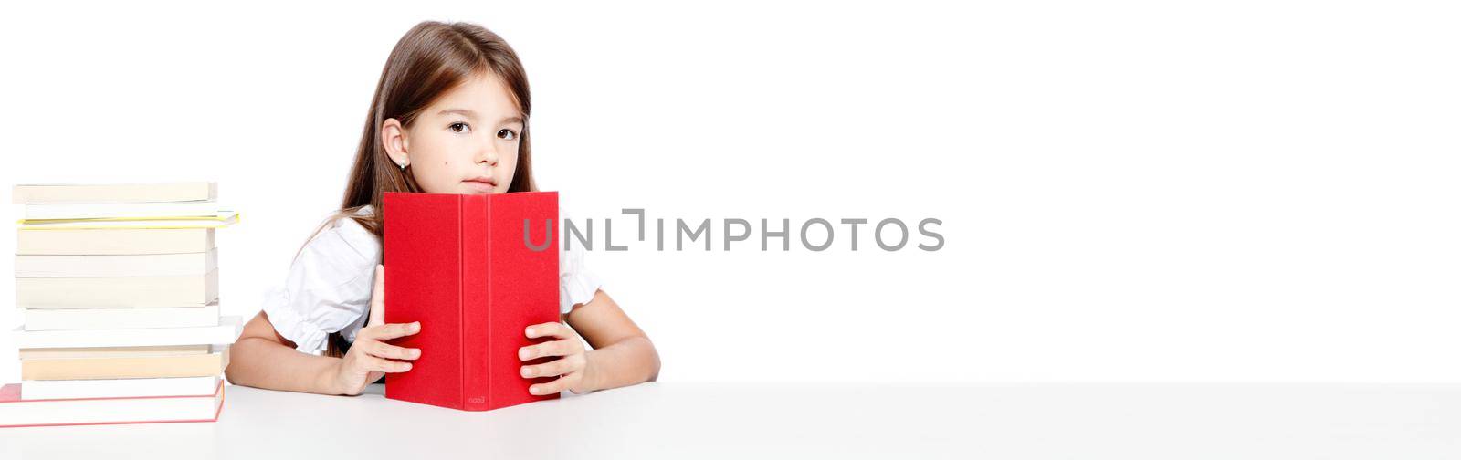 Young cute girl sitting at the table and reading a book by Taut