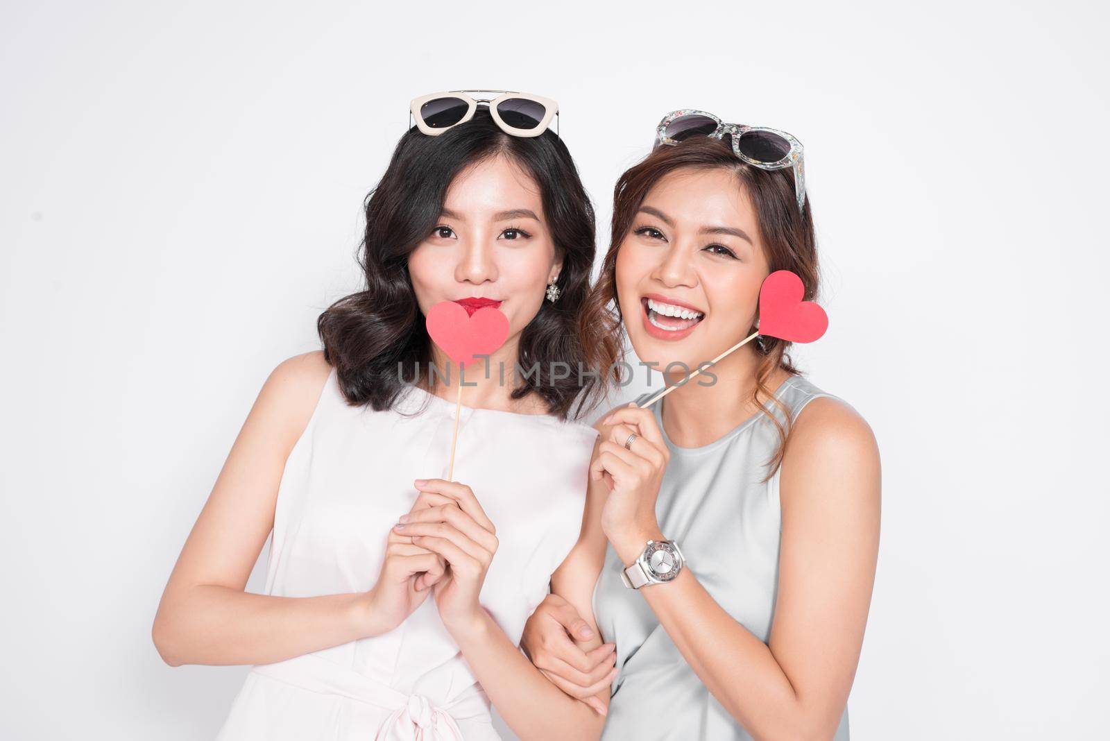 Two fashionable women in nice dresses standing together and holding red heart shape.