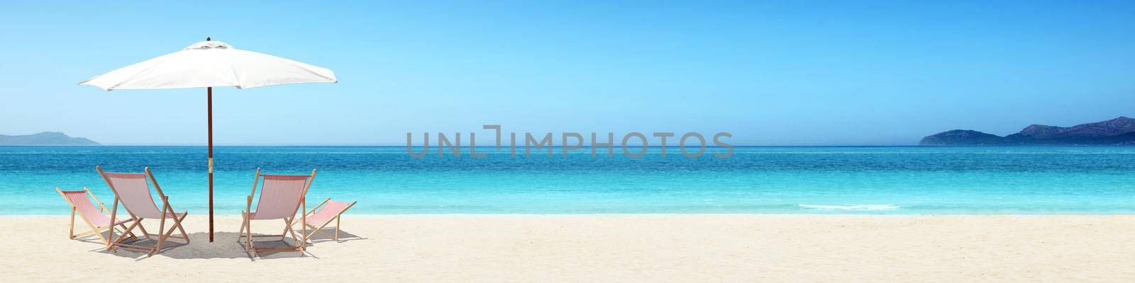 Wooden deck chairs on sandy beach near sea. Holiday background.