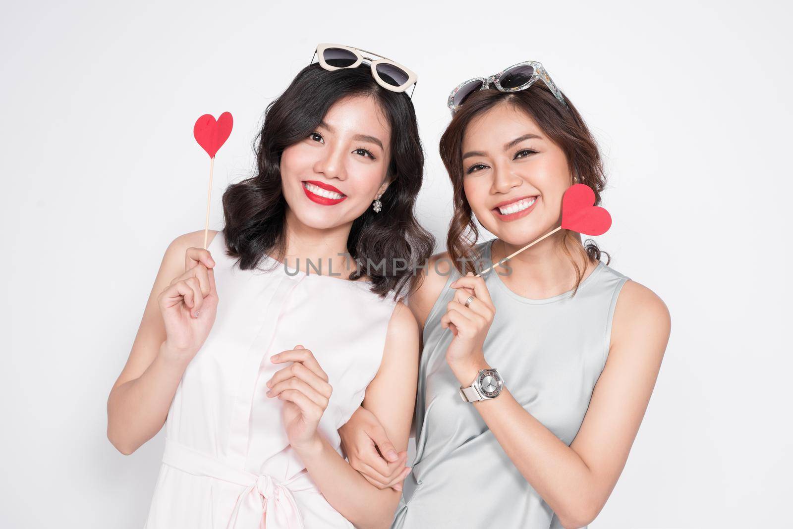 Two fashionable women in nice dresses standing together and holding red heart shape. by makidotvn