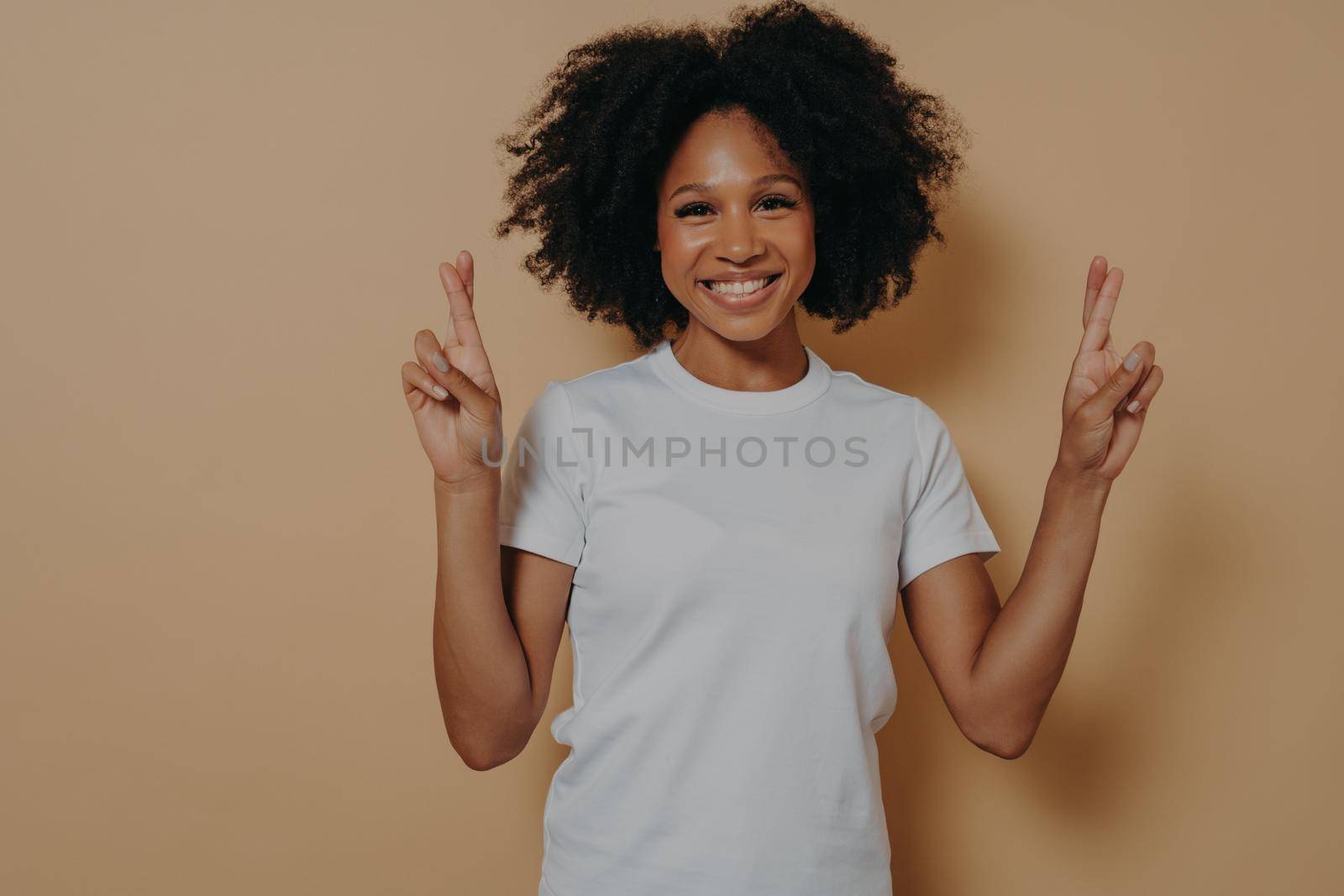 Hopeful african american female isolated on beige studio background crossing fingers making wish by vkstock