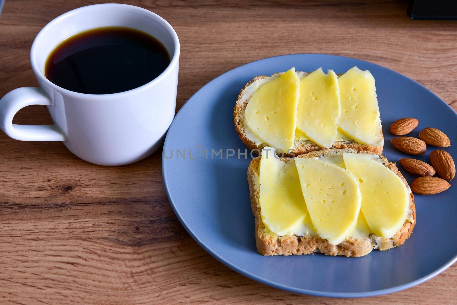 A cup of coffee, toast with cheese and almonds on a plate, stand on a wooden table by karpovkottt