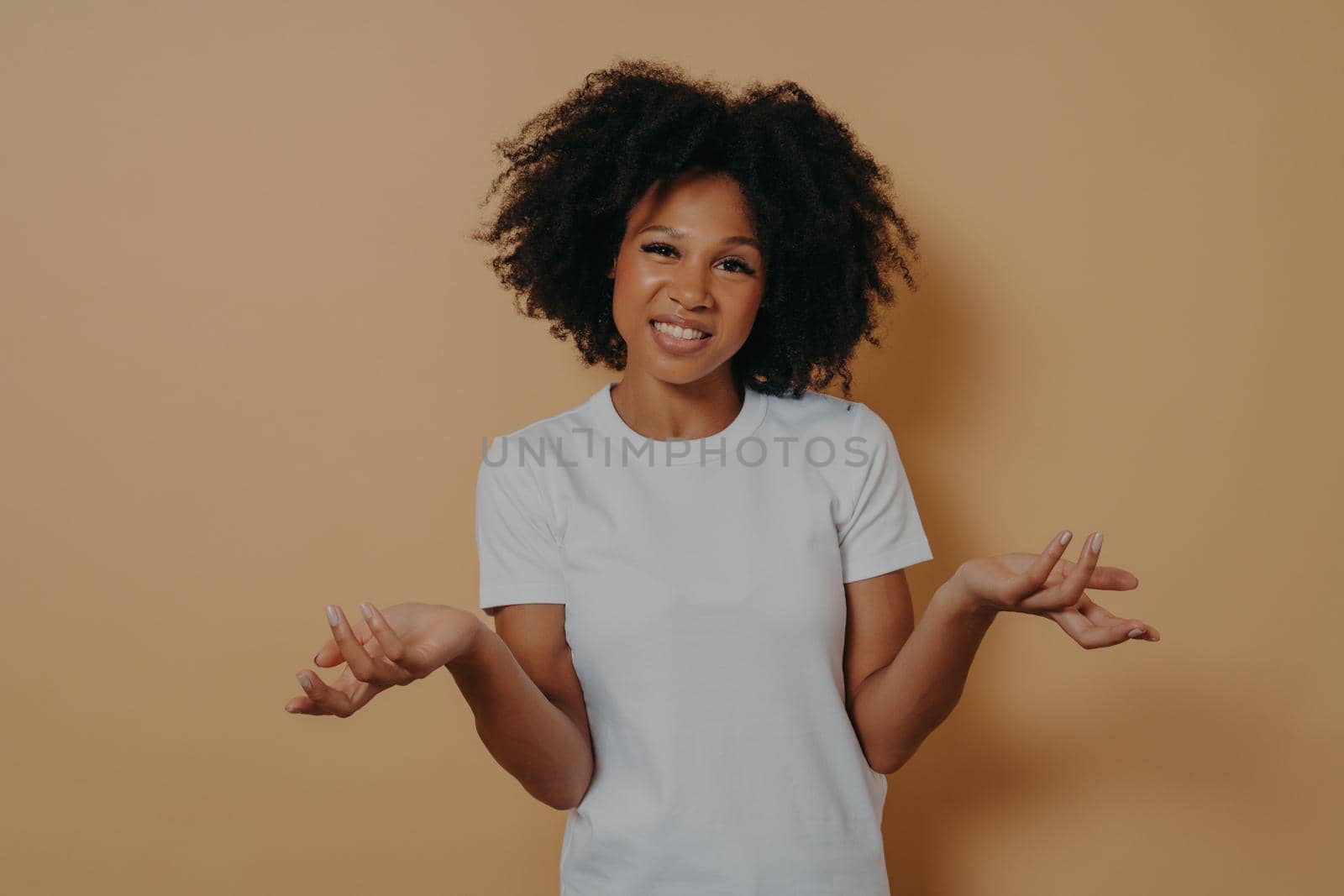 Confused african female can not make decision, shrugging shoulders isolated on beige background by vkstock