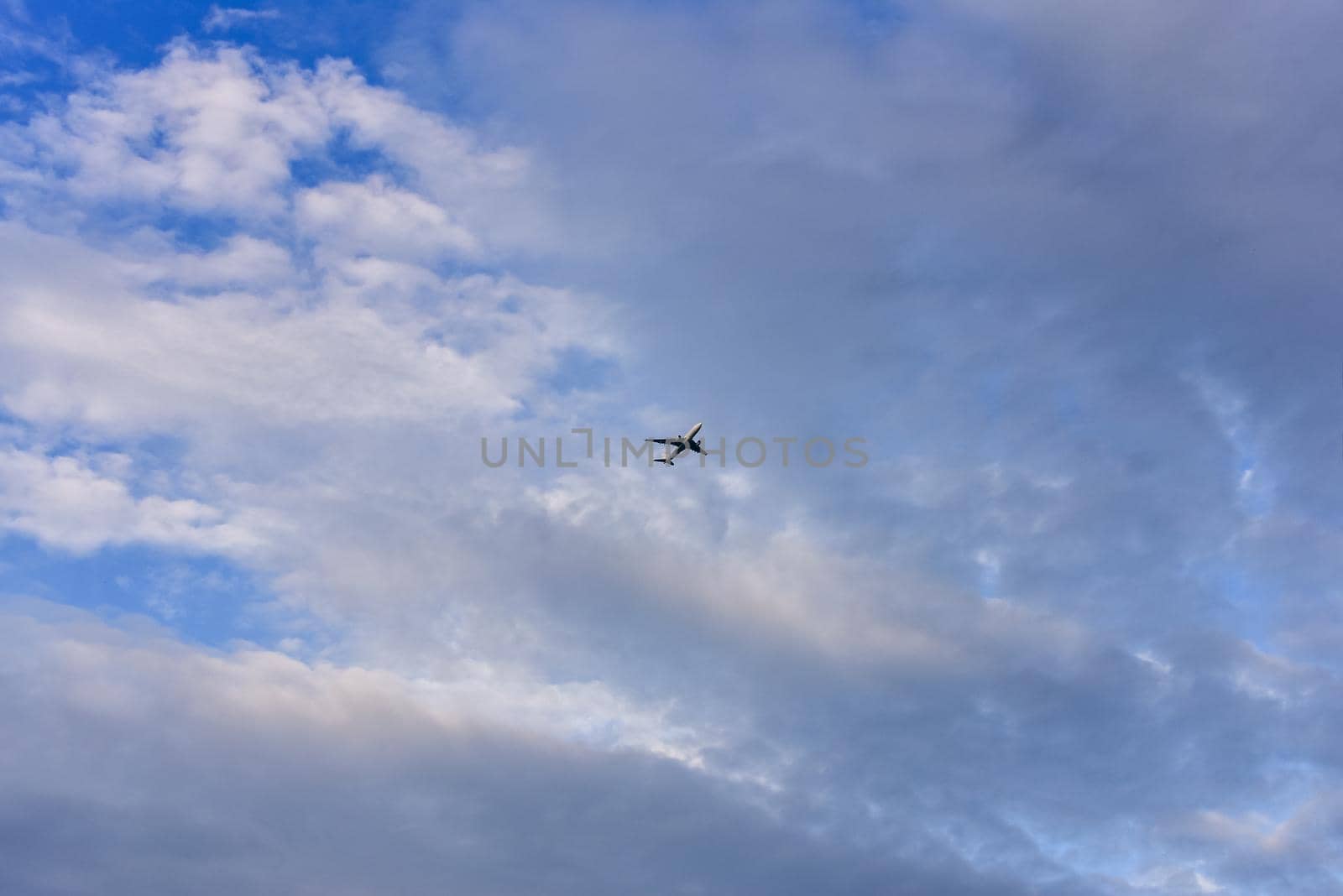 Passenger plane is flying far away against the blue summer and cloudy sky.