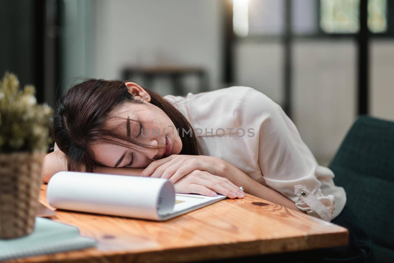 Tired and overworked business woman. Young exhausted girl sleeping on table during her work Entrepreneur, freelance worker or student in stress concept by nateemee