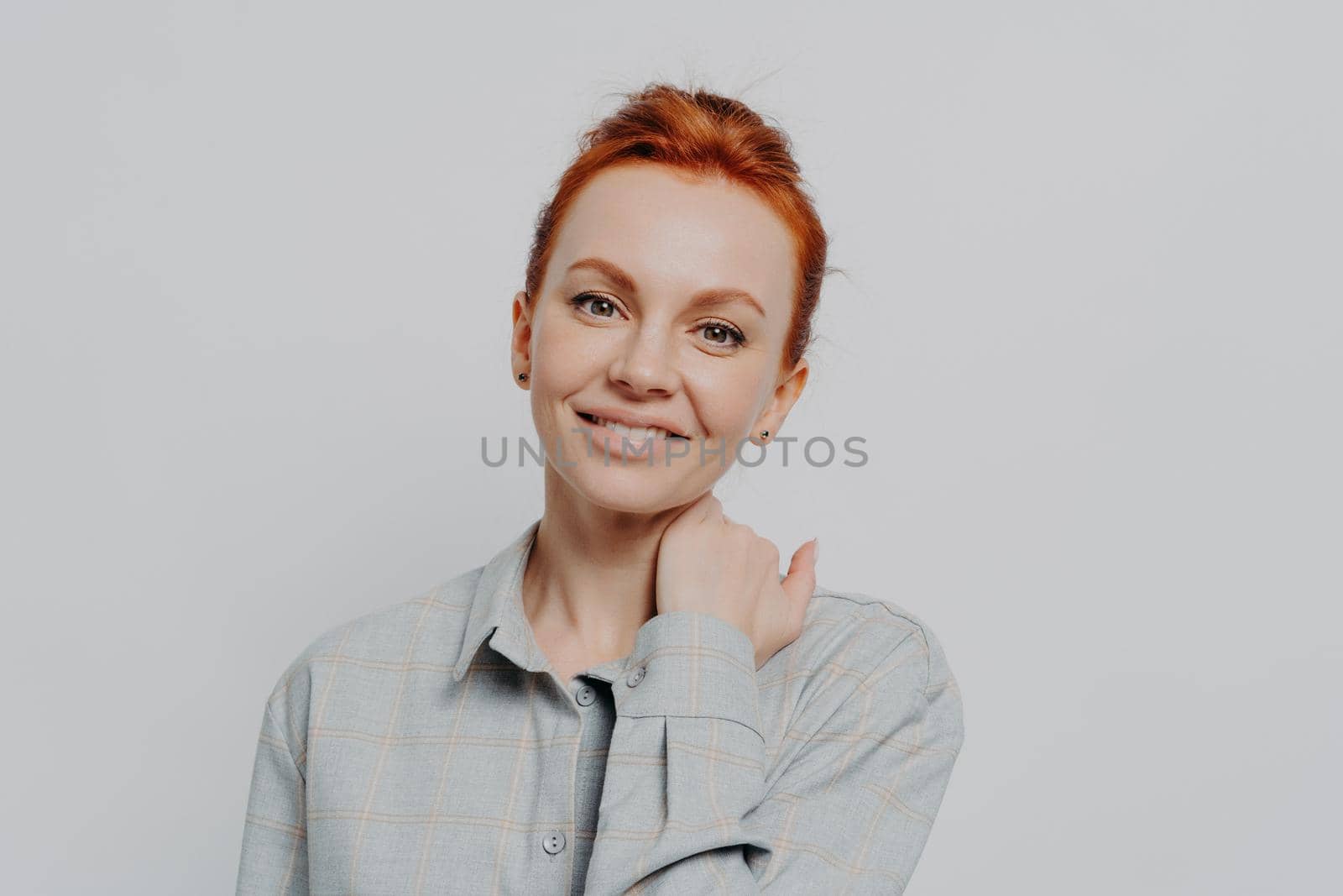 Young attractive smiling female with ginger hair in casual outfit isolated on grey studio background, happy caucasian woman with beaming smile looking at camera, posing indoors