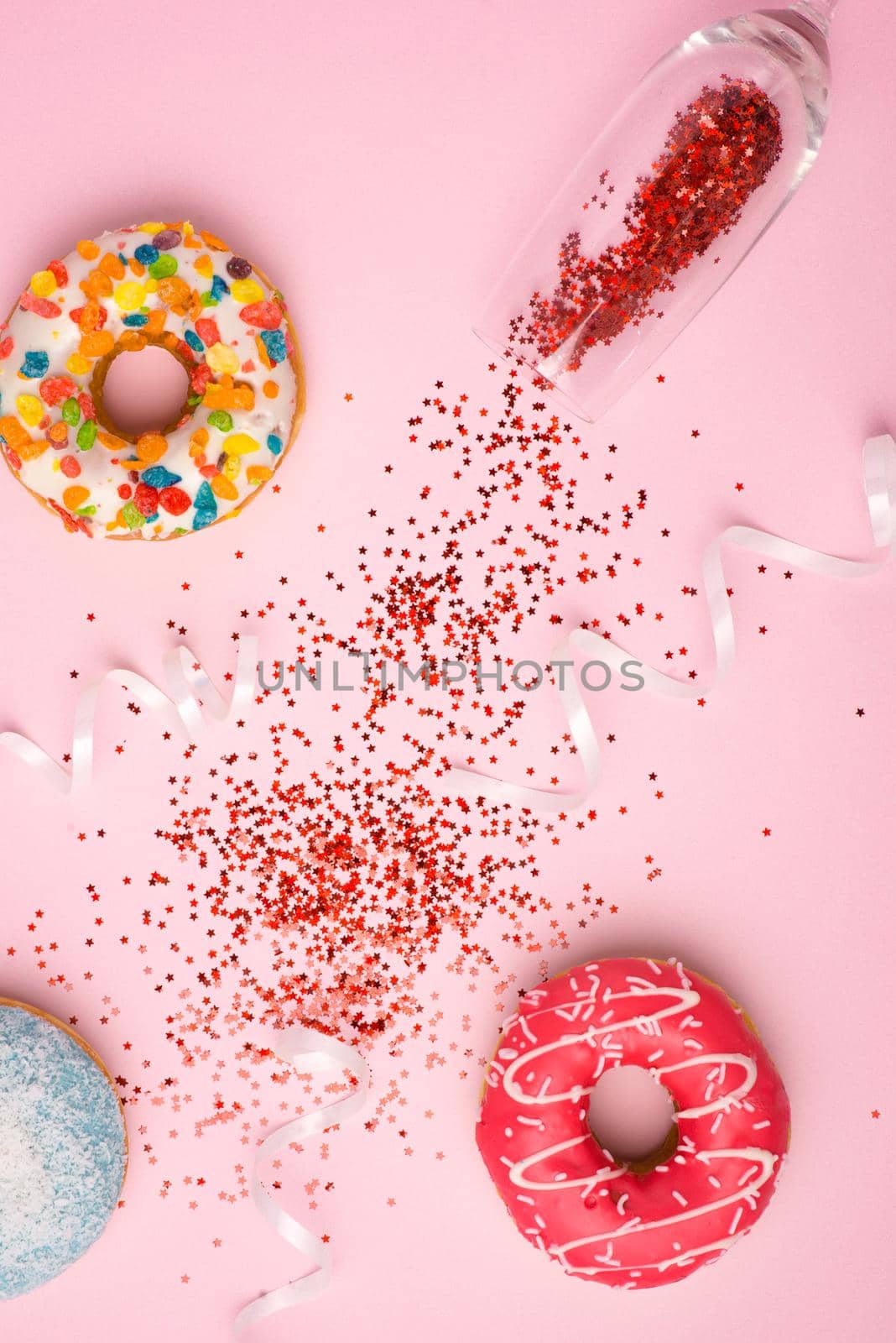 Flat lay of Celebration. Champagne glass with colorful party streamers and delicious donuts on pink background.