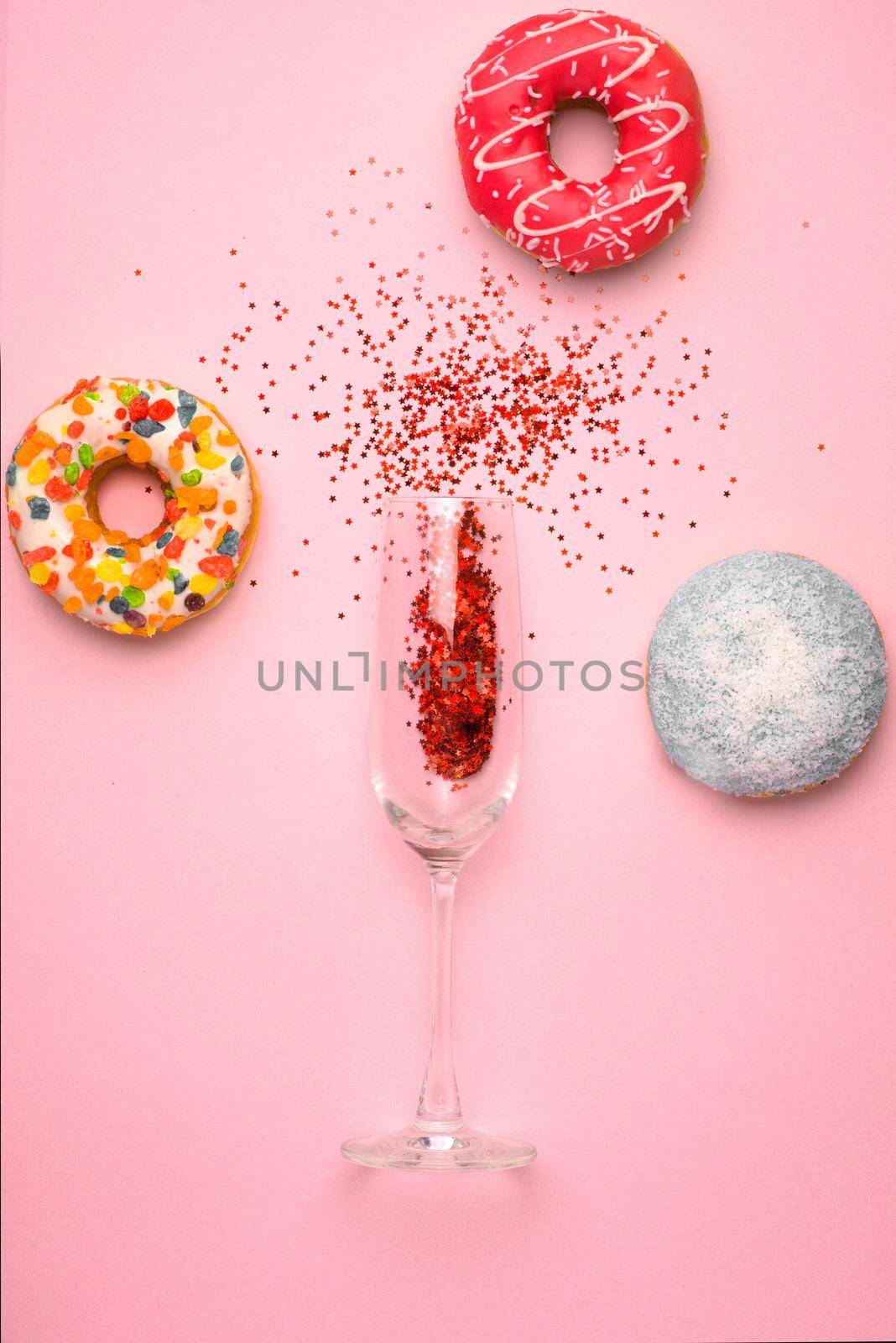 Flat lay of Celebration. Champagne glass with colorful party streamers and delicious donuts on pink background.