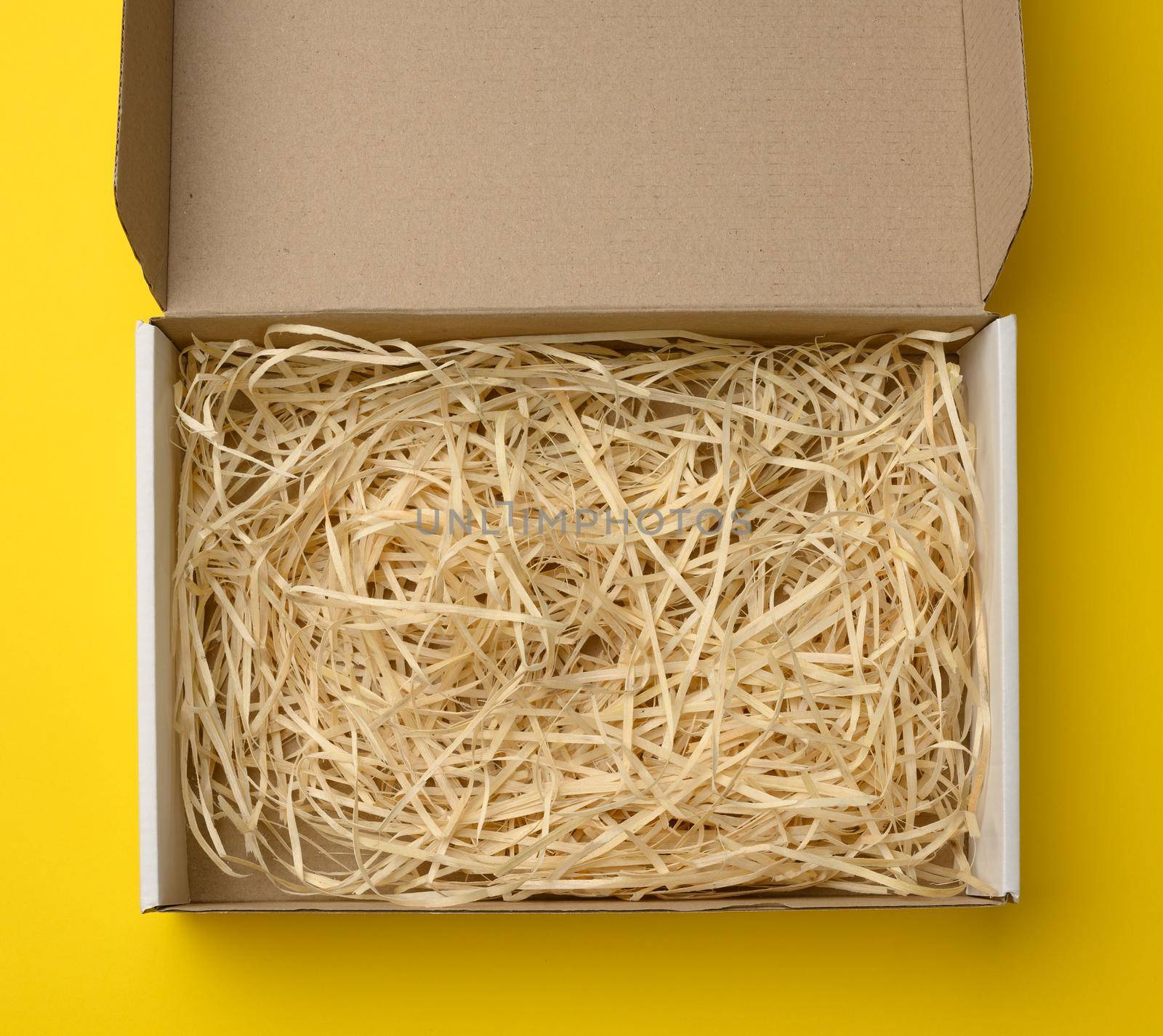 empty rectangular open corrugated paper box with sawdust inside. Packaging, containers for transportation on a yellow background
