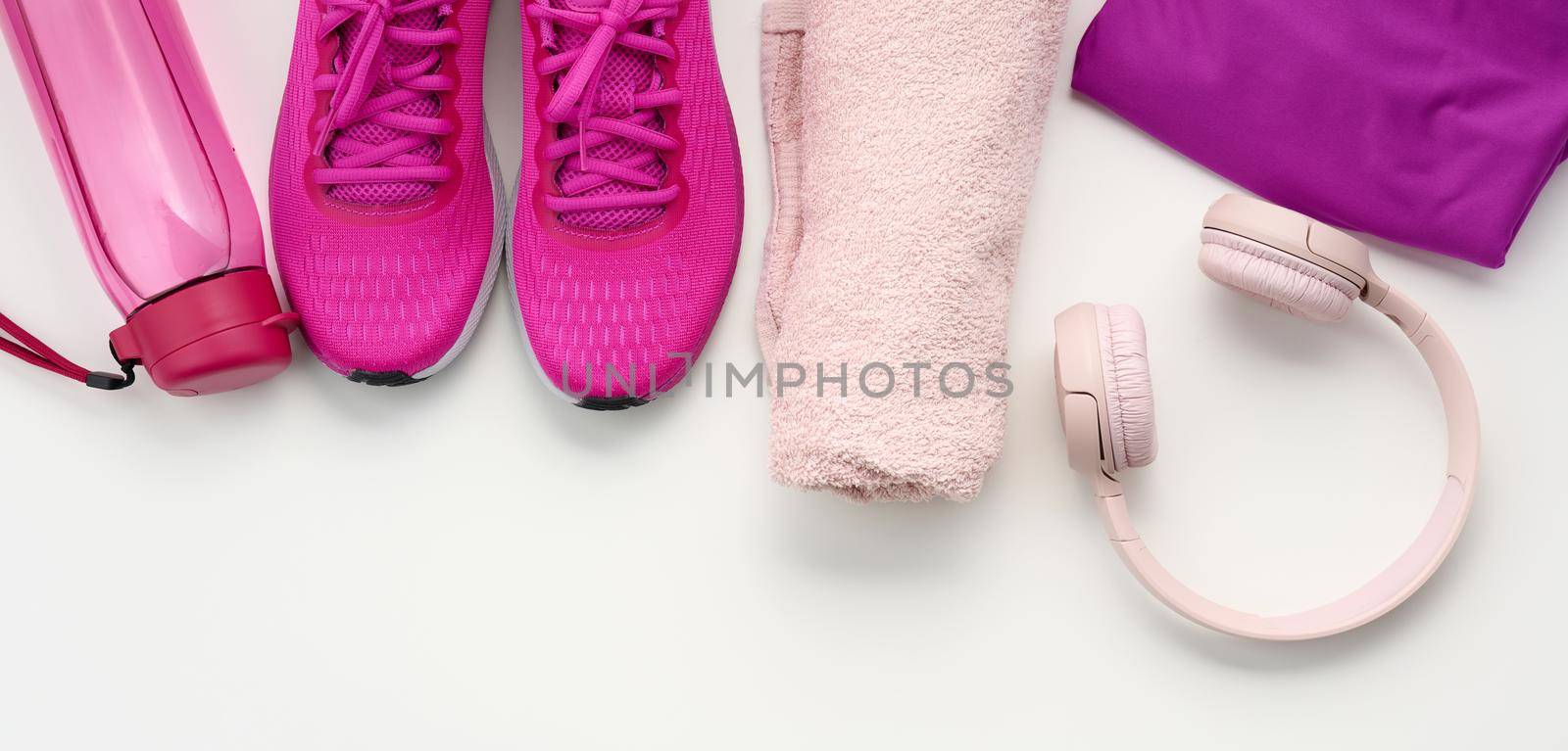 a pair of textile purple sports sneakers, wireless headphones, a towel and a bottle of water on a white background by ndanko