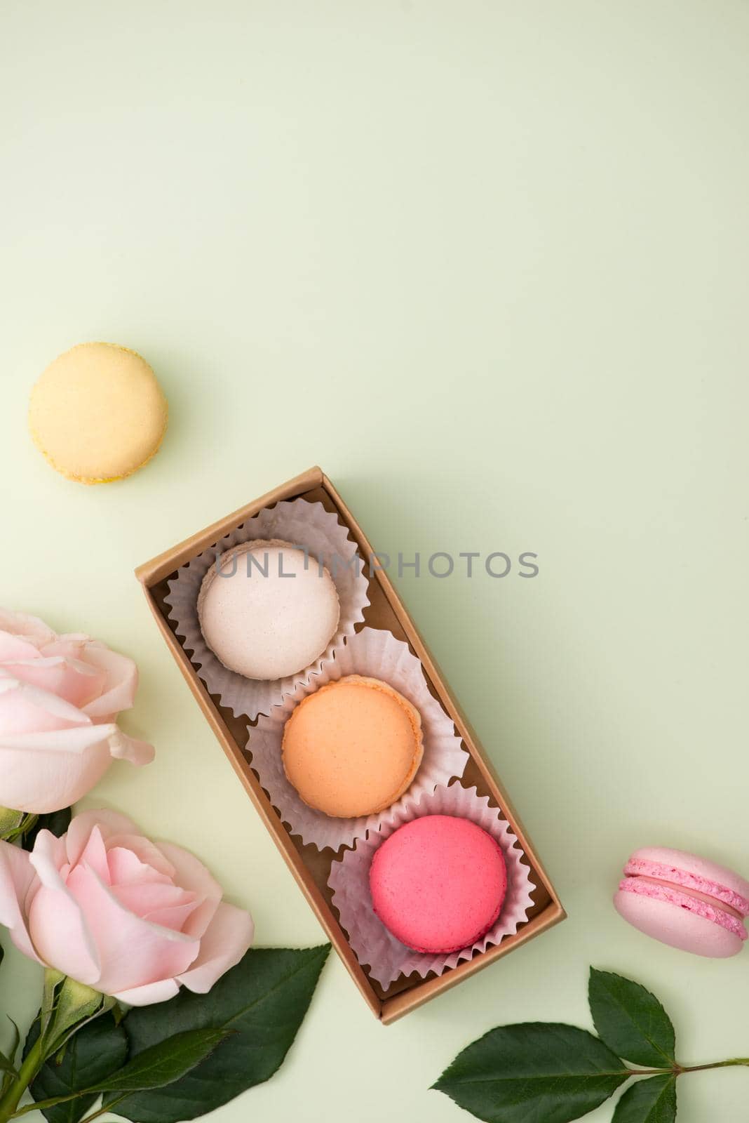 French macaroons. Many variegated sweet macarons in box with bouquet of pink roses on the table