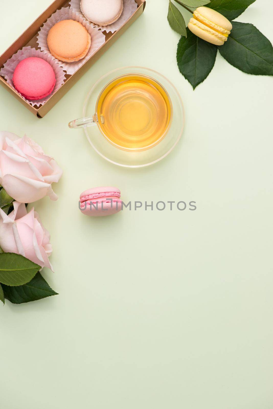 French macaroons. Many variegated sweet macarons in box with bouquet of pink roses on the table