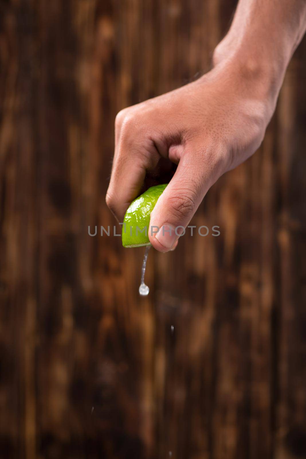 Hand squeeze lime with lime drop on dark wooden background