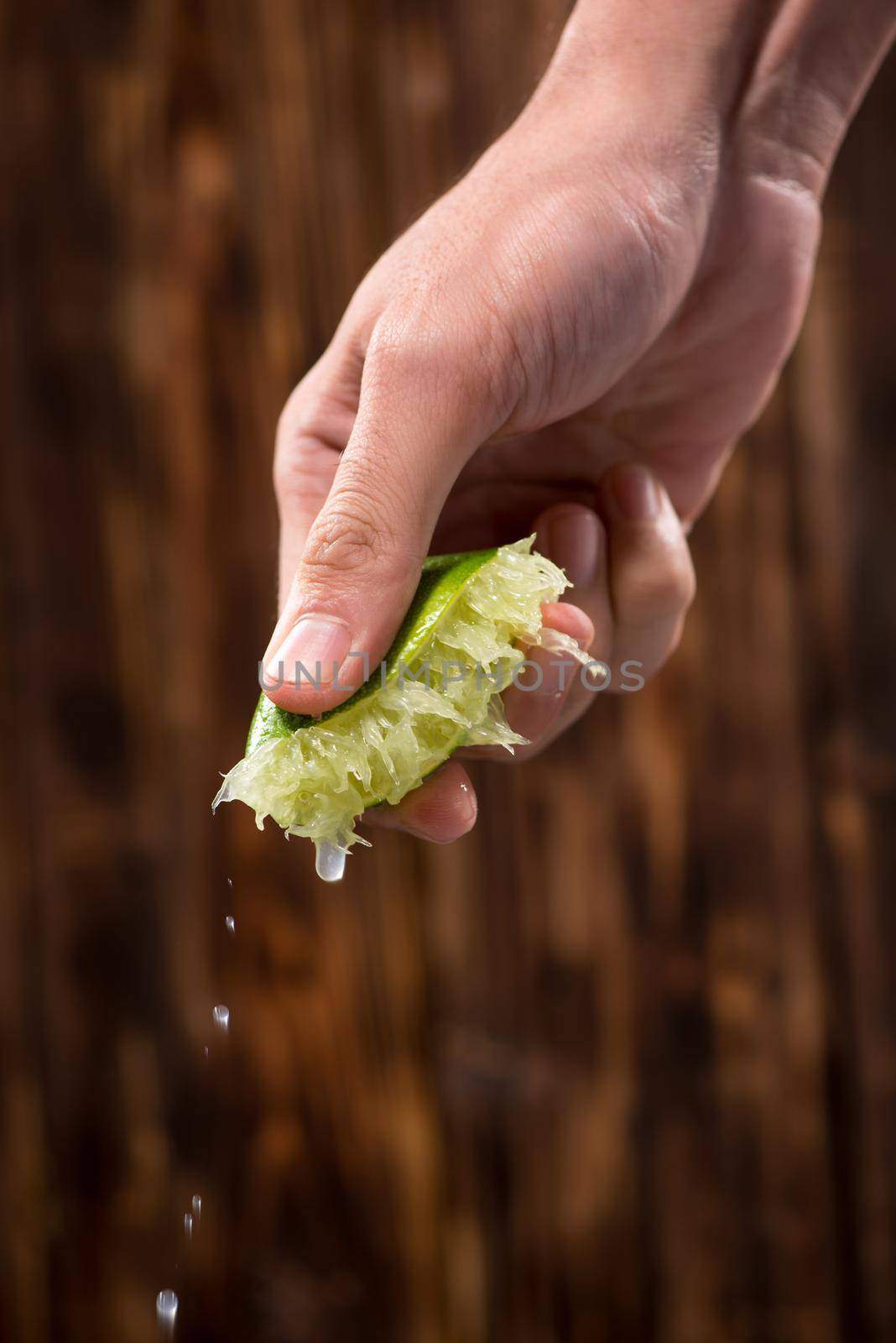 Hand squeeze lime with lime drop on dark wooden background