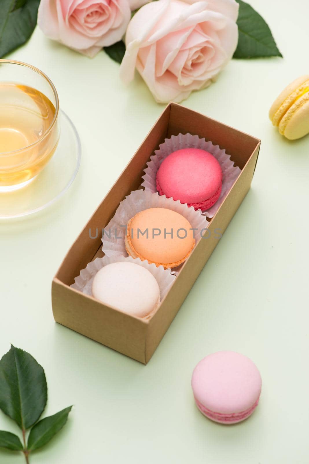 French macaroons. Many variegated sweet macarons in box with bouquet of pink roses on the table
