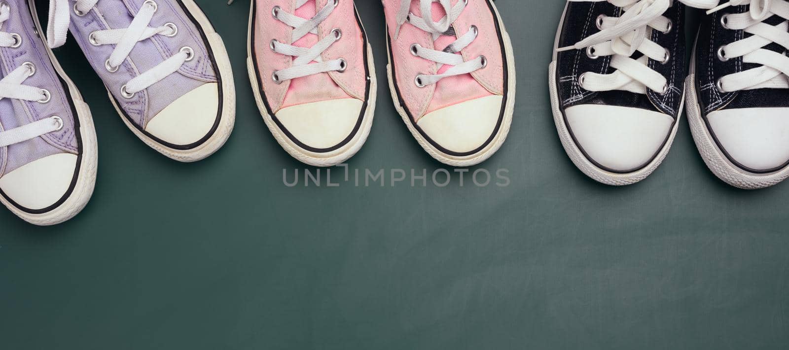 a lot of used textile sneakers on a green background, various sizes. Family concept, friendship, top view, copy space